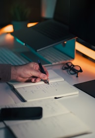 Hand writing notes in a notebook at a desk.