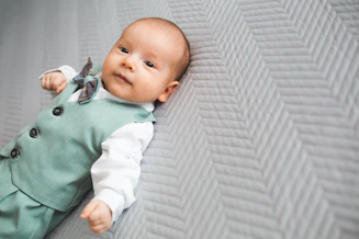 A baby in a suit lies on a patterned surface