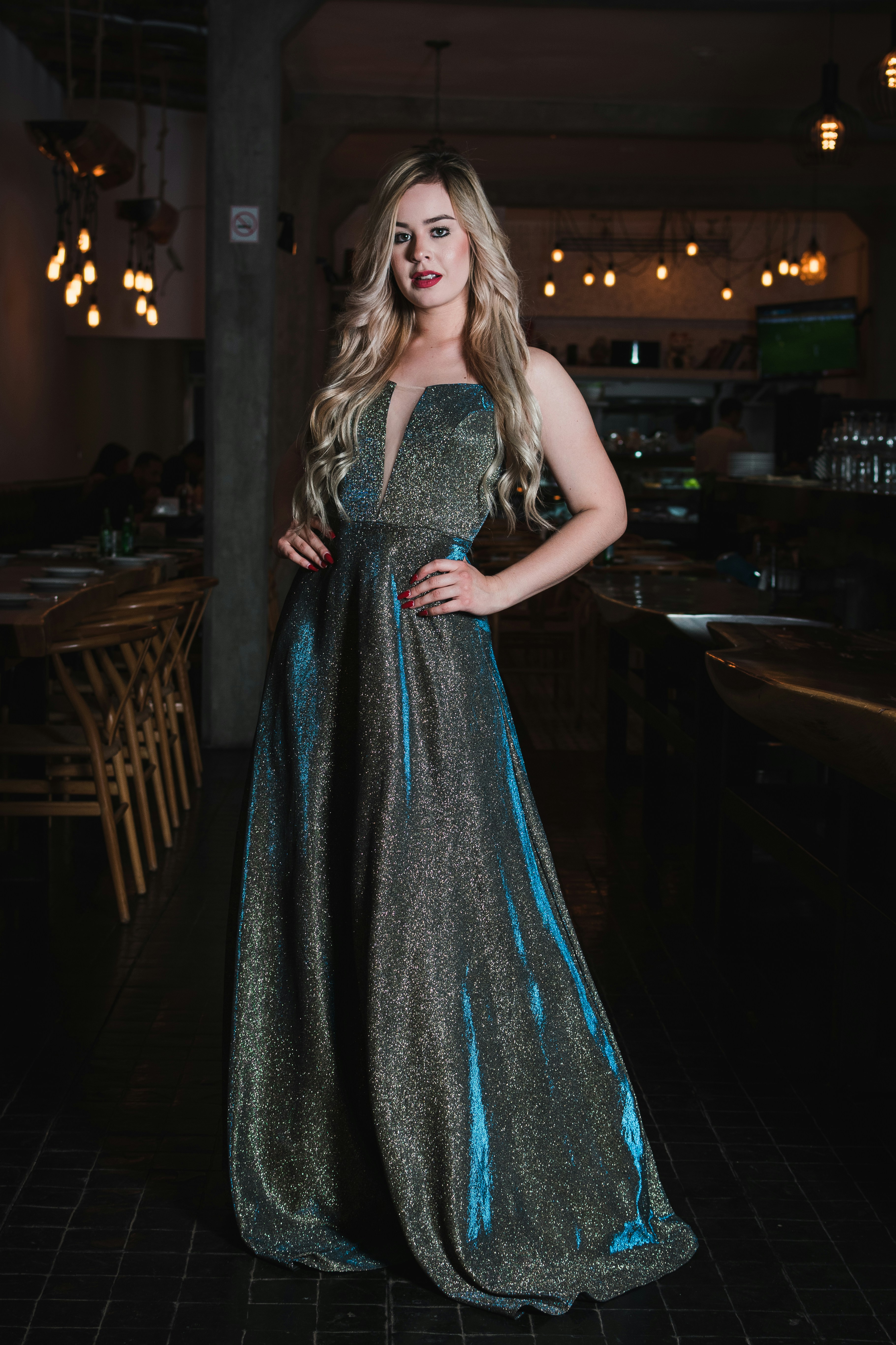 Uma mulher em um vestido de noite azul cintilante em um restaurante mal iluminado