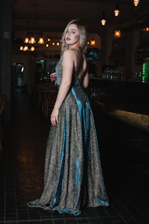 A woman in a shimmering blue gown looking back in a dimly lit restaurant.