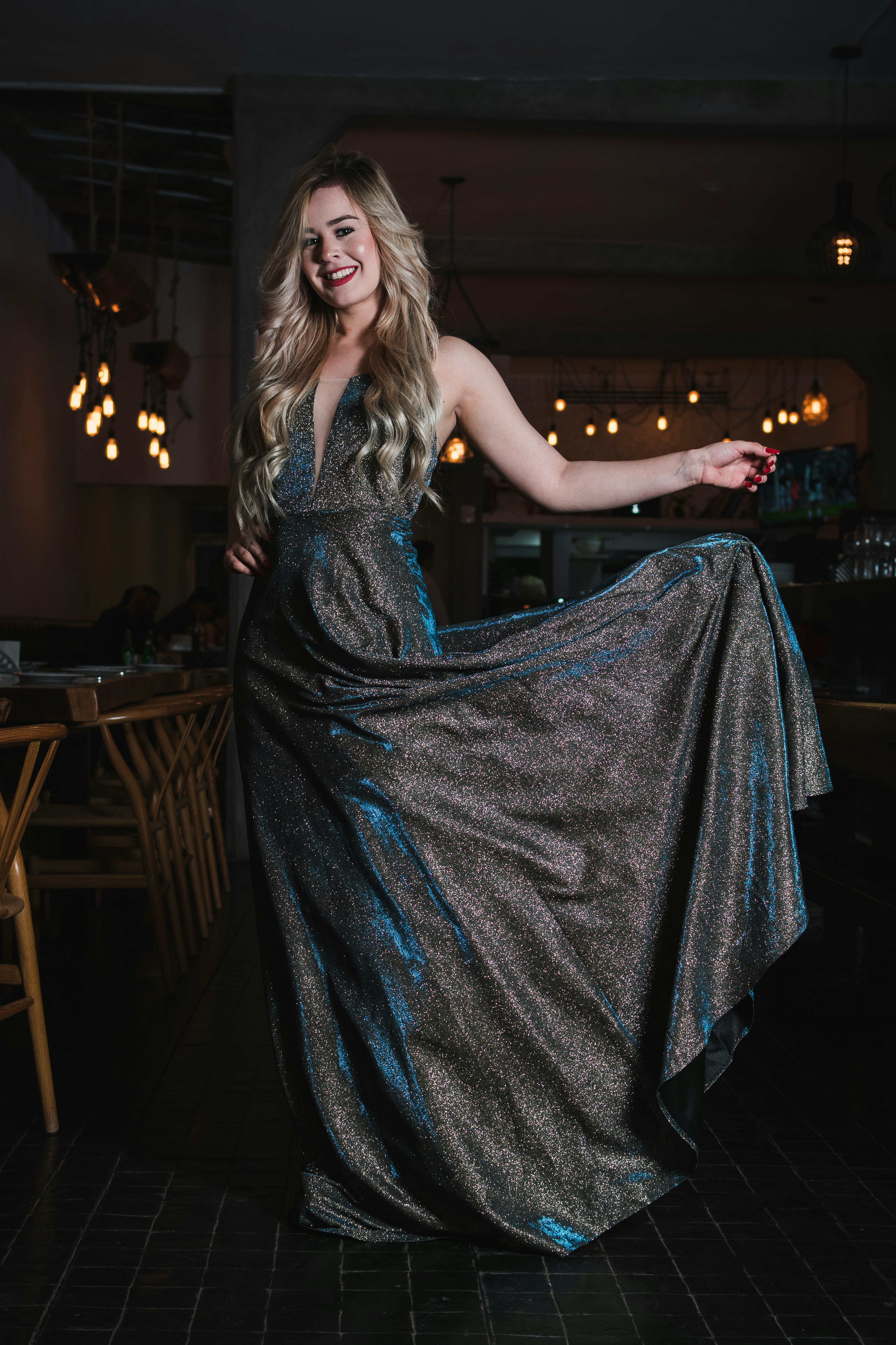 A woman in a shimmering dark gown posing in a dimly lit restaurant.