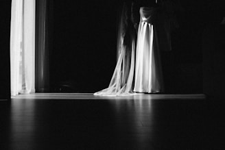A white wedding dress hangs in a dark room.