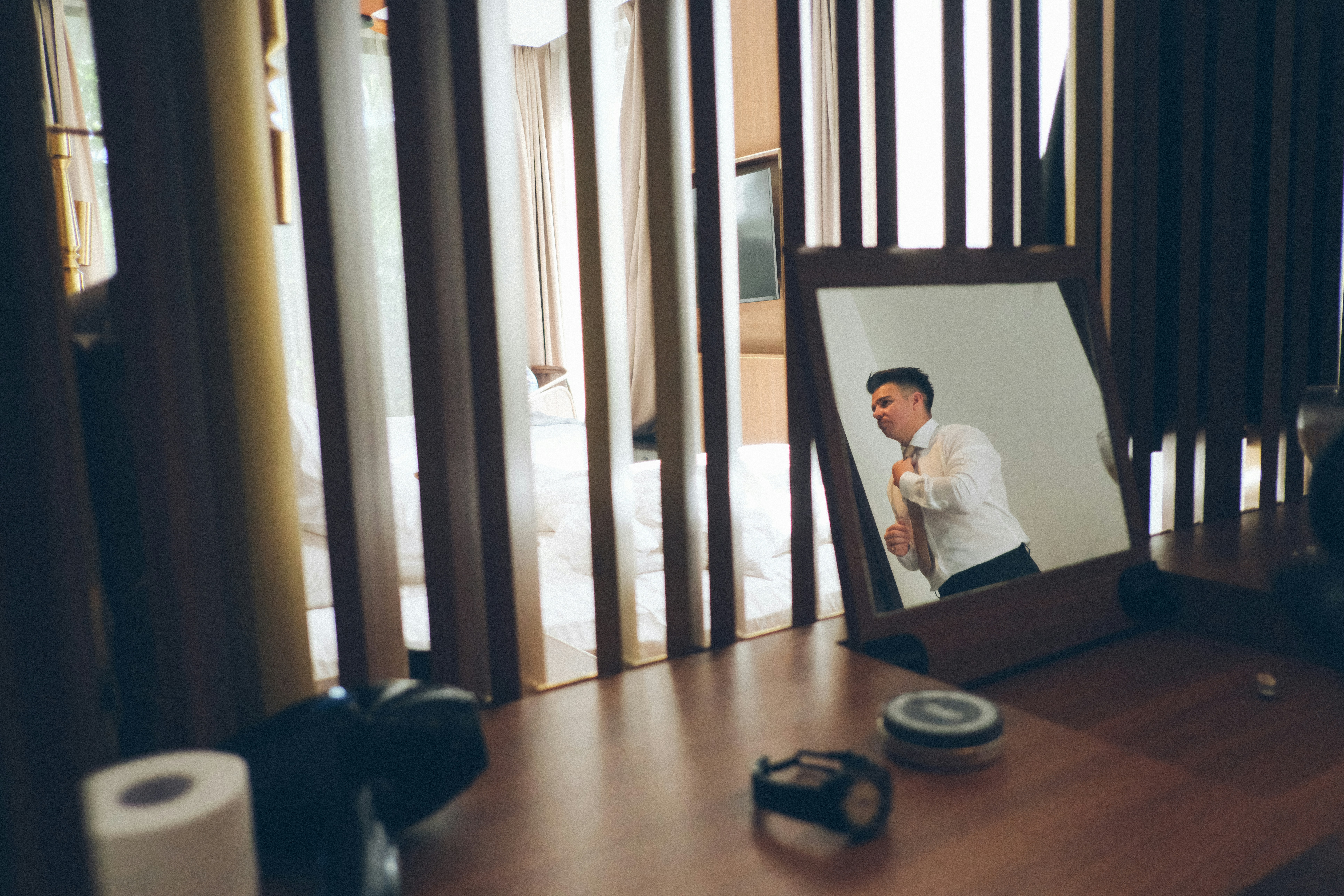 Man in white shirt tying necktie in mirror reflection