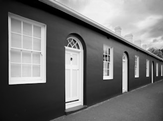 Row of dark buildings with white windows and doors.