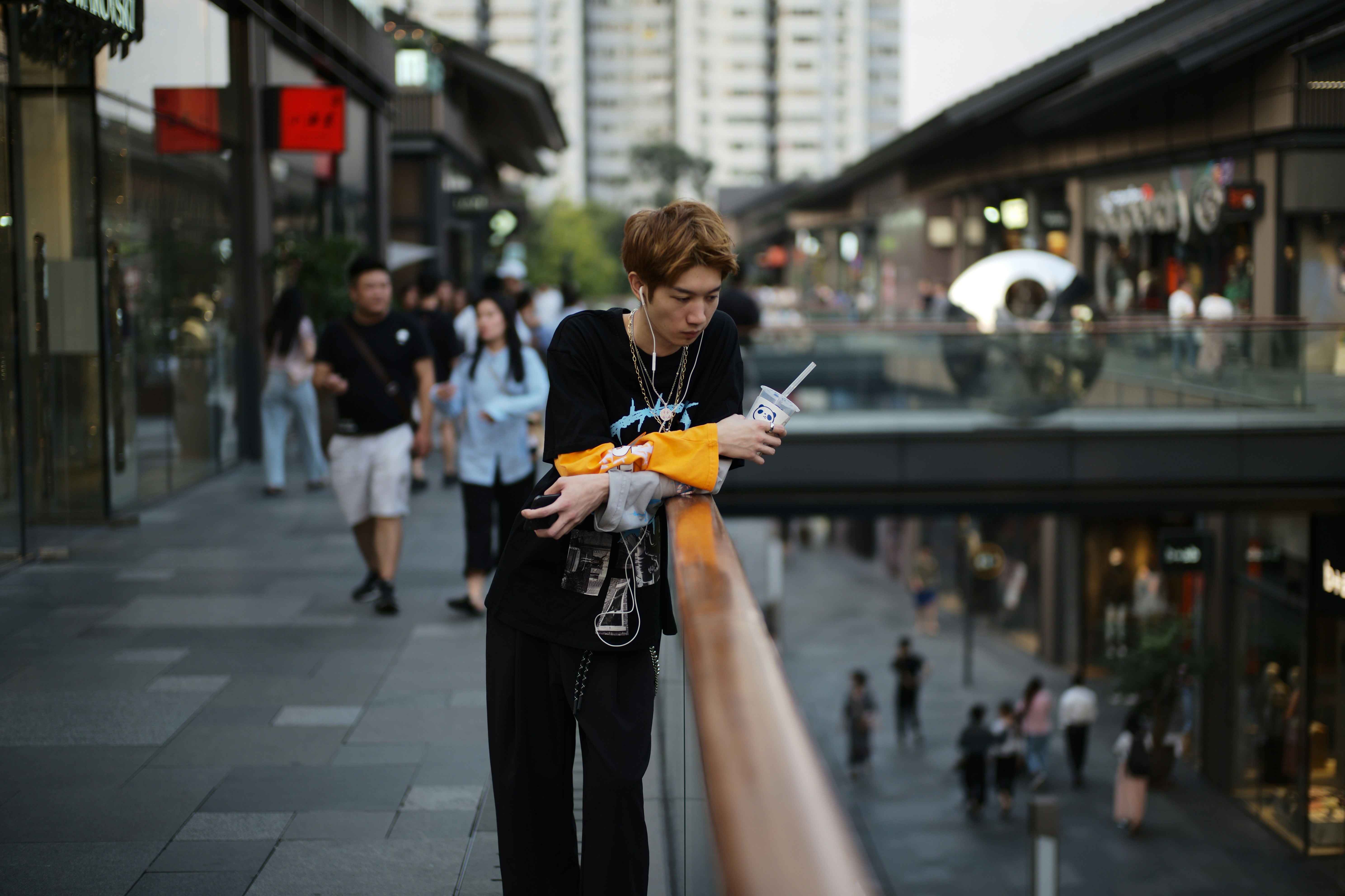 Man leaning on railing in a bustling outdoor shopping area.
