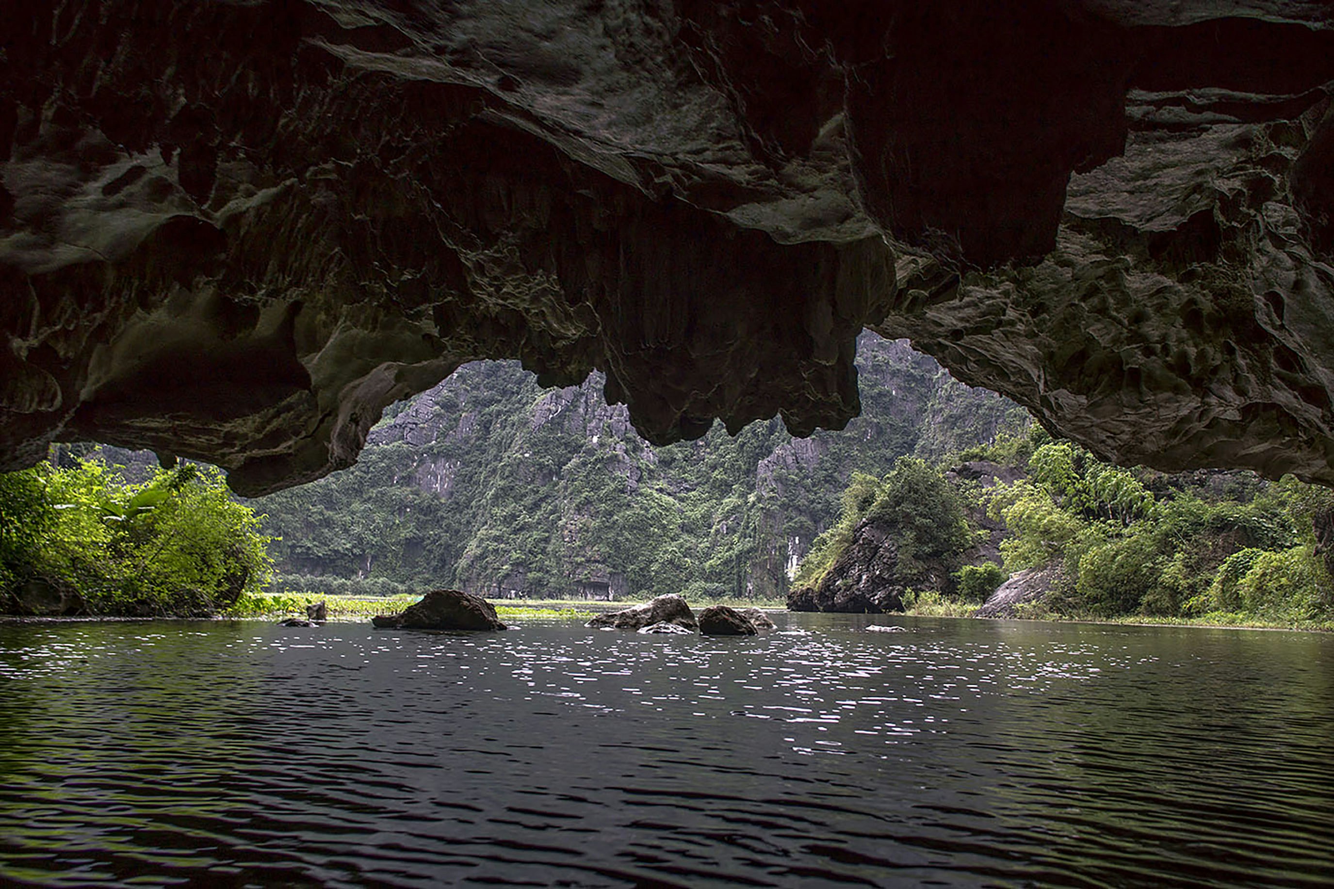 A river flows through a cave towards lush green mountains.