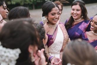 Bride smiles surrounded by her friends in traditional indian attire.
