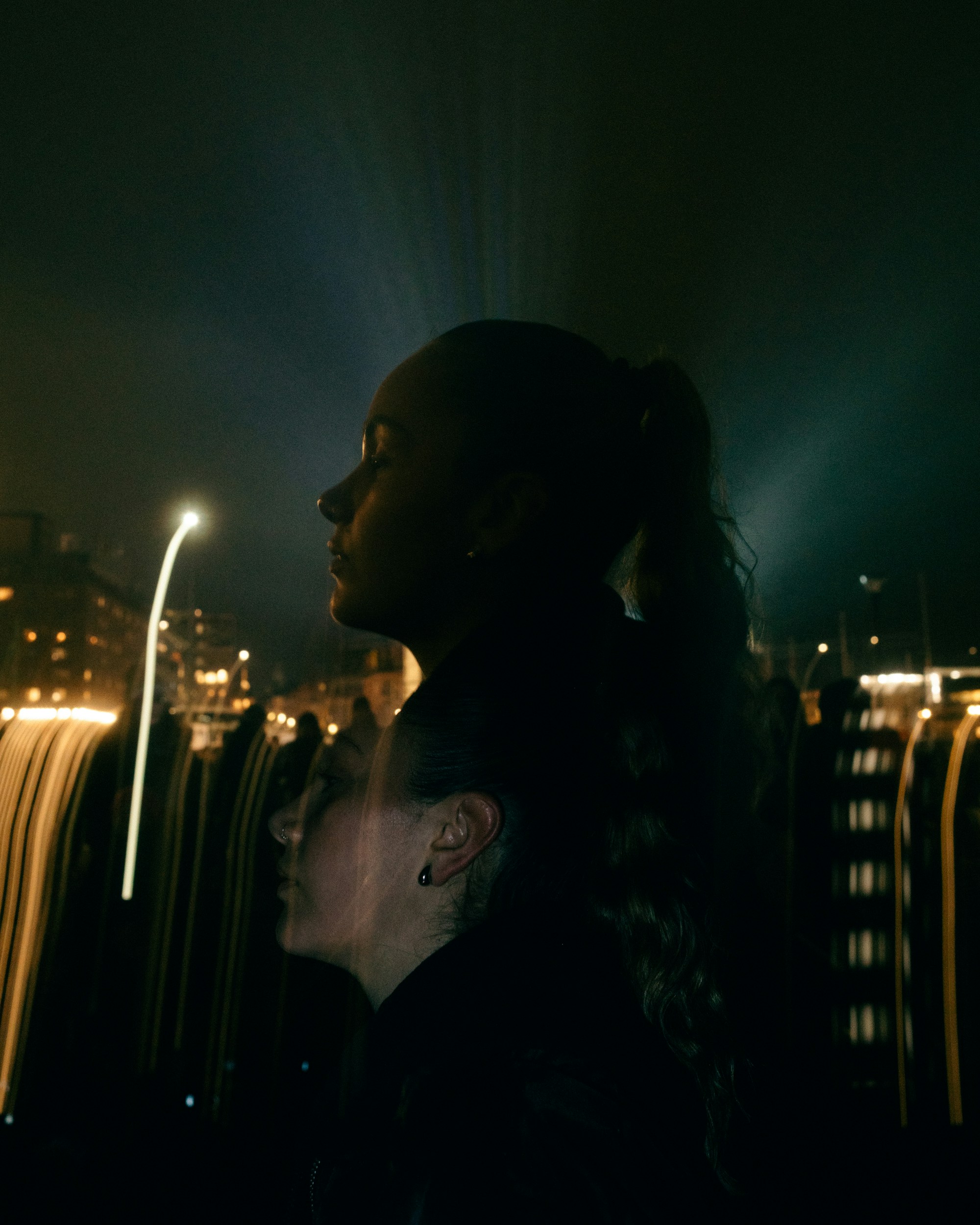 Two women silhouetted against a blurred city lights background.
