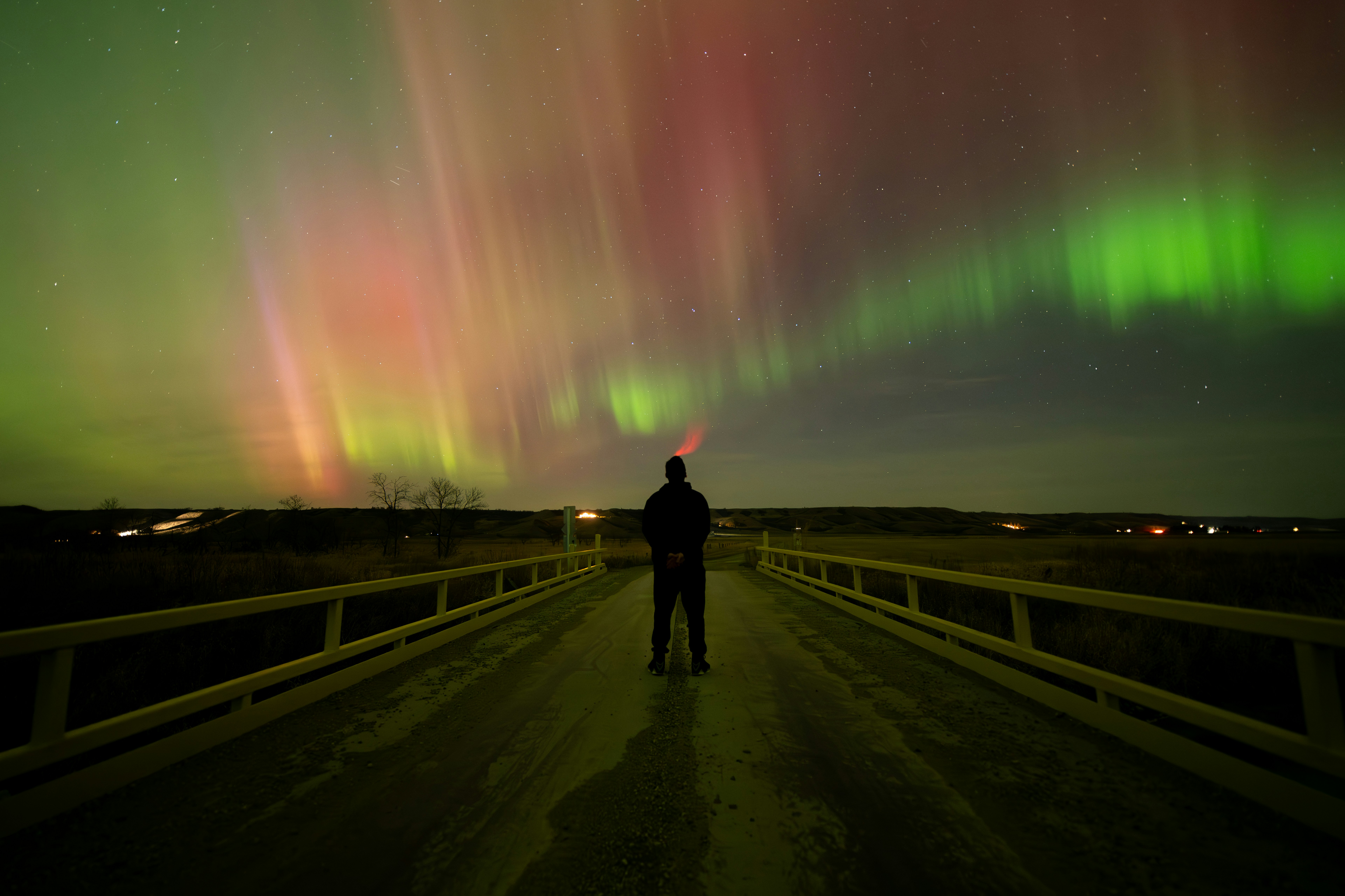 Person standing on bridge watching aurora borealis lights.
