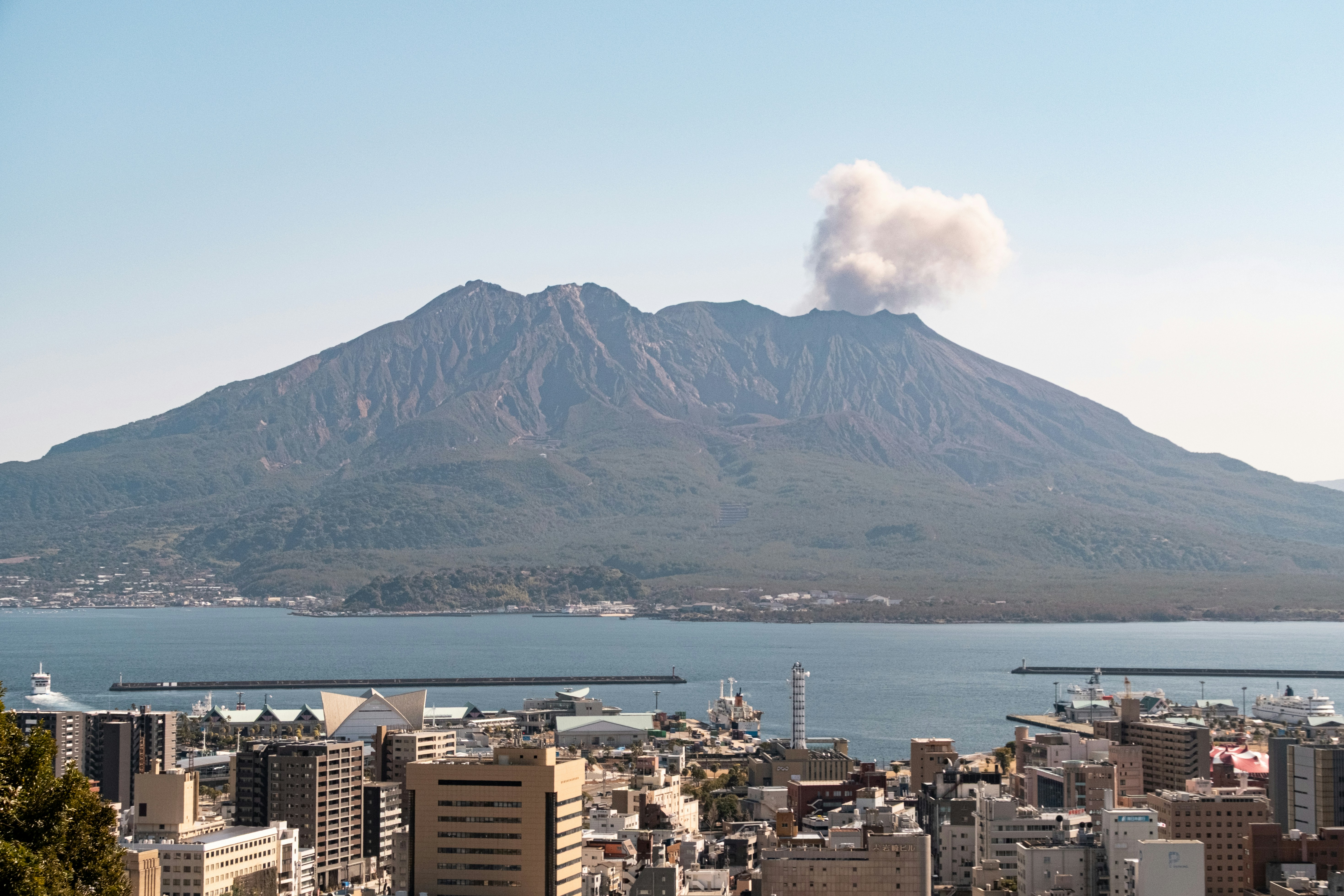 Volcano erupting smoke over a coastal city.