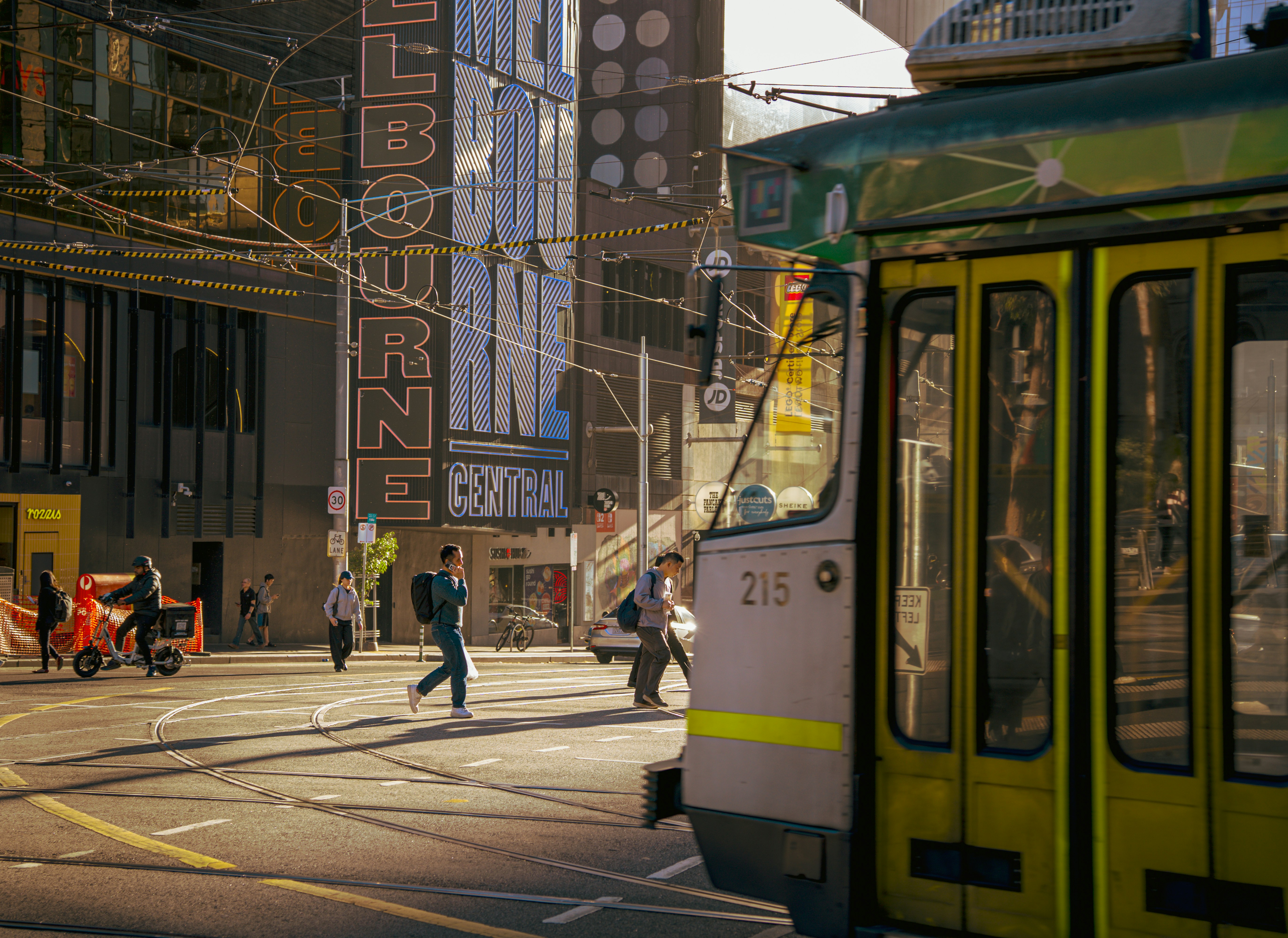 A yellow tram on a city street with pedestrians.