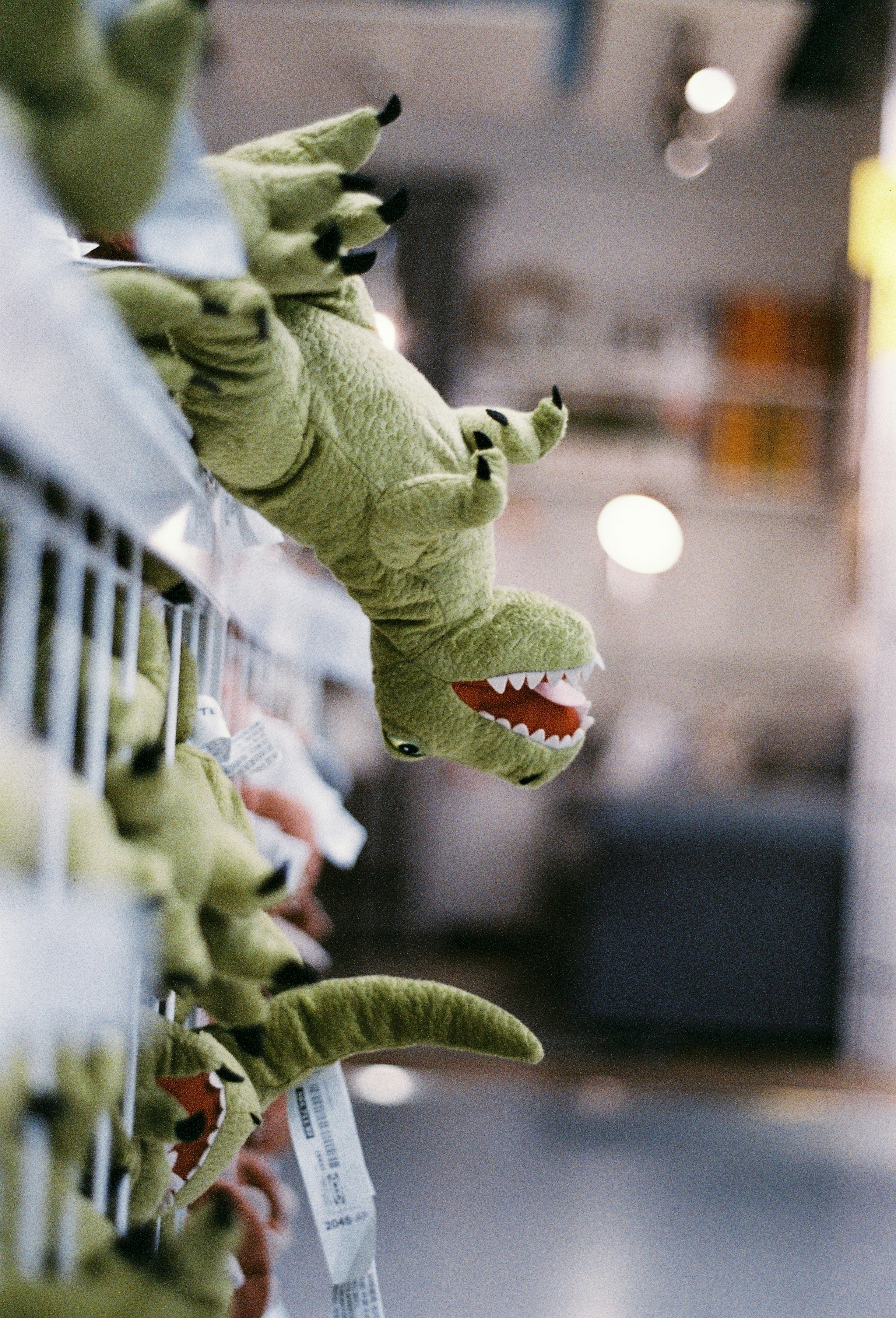 Green plush dinosaur toys hang from a metal display rack.