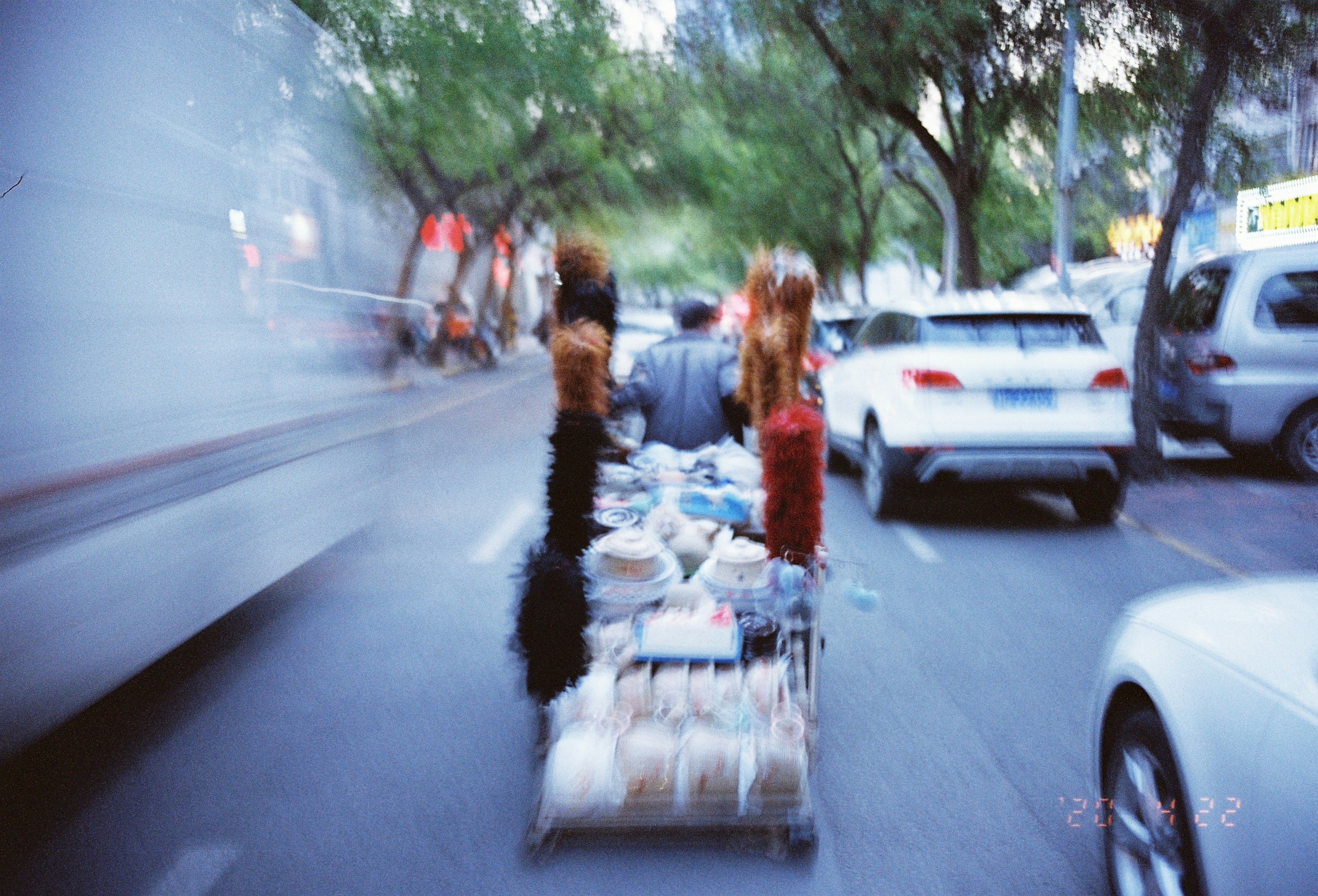 Street vendor pushing cart with goods on busy road.