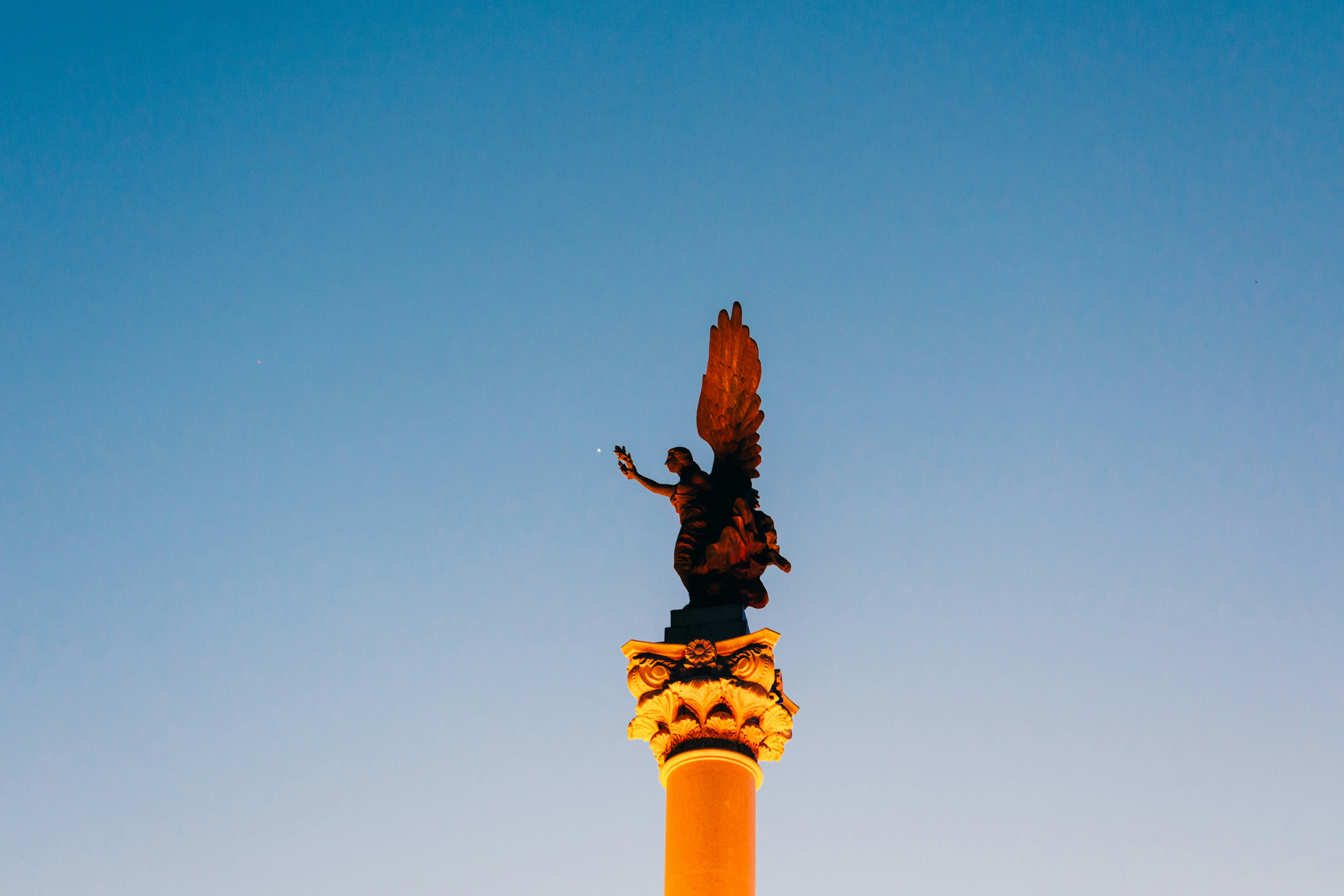 Statue of winged figure atop ornate column against blue sky