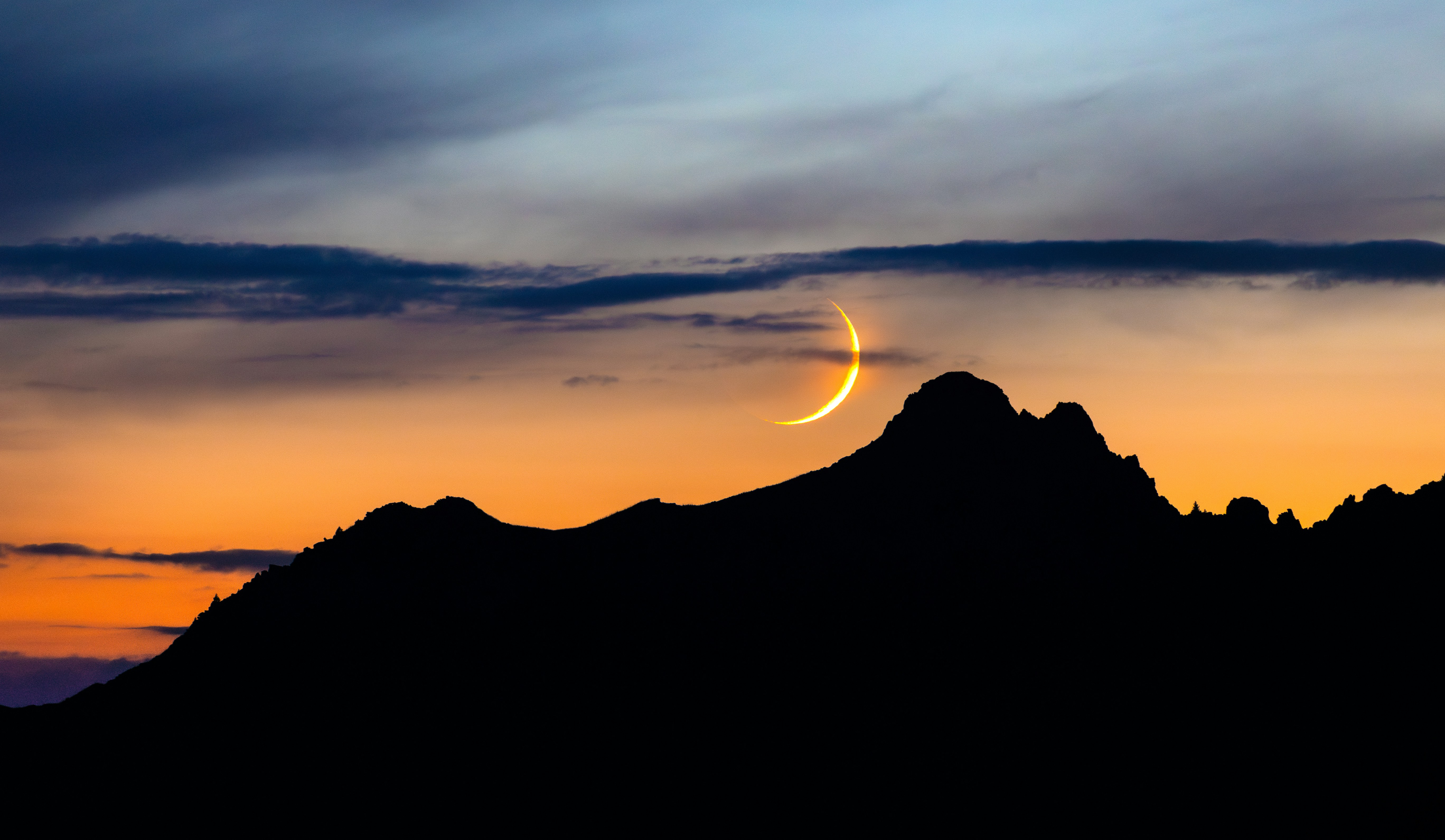 Crescent moon over silhouetted mountains at sunset