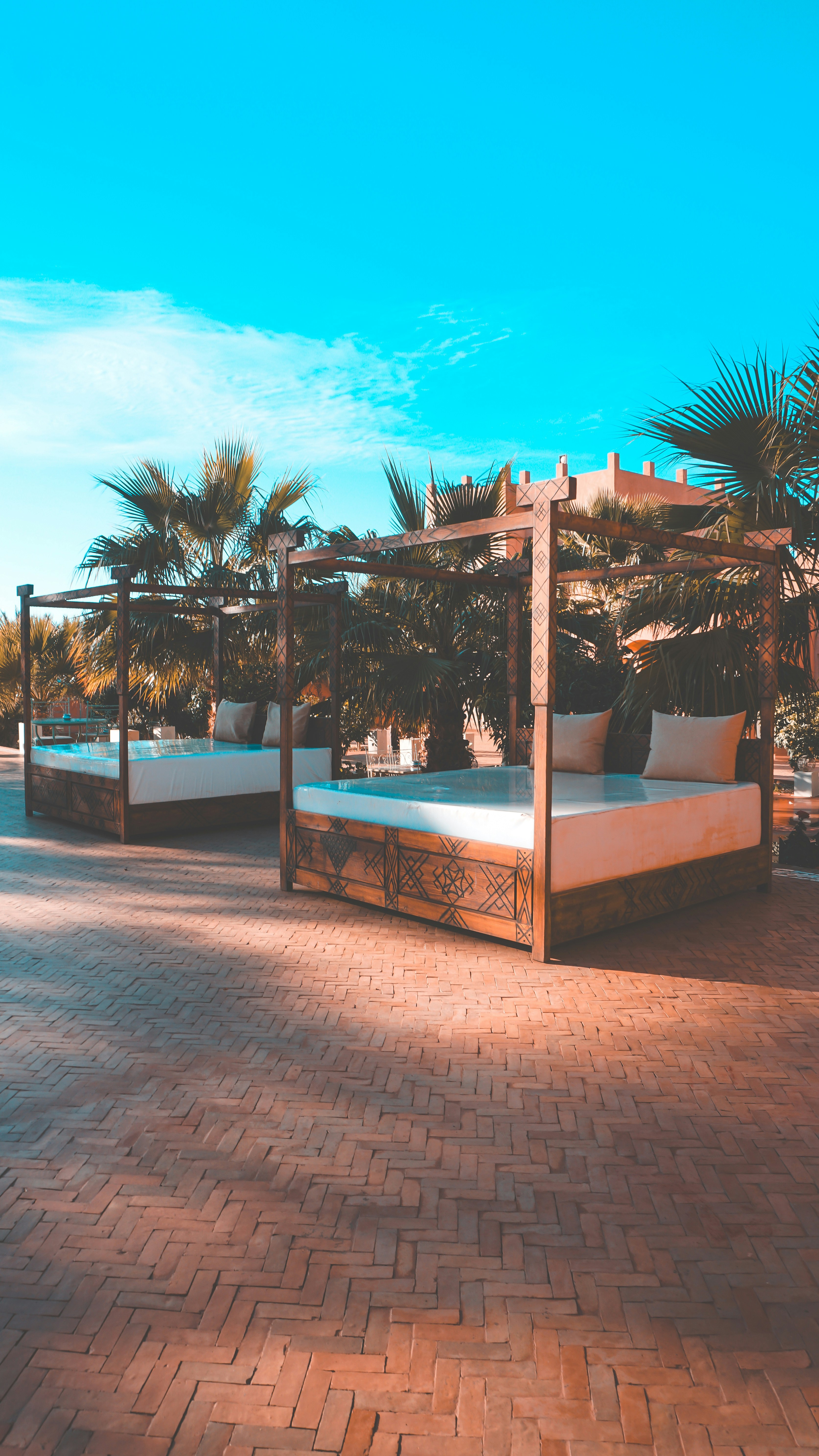 Two canopy beds on a brick patio with palm trees.
