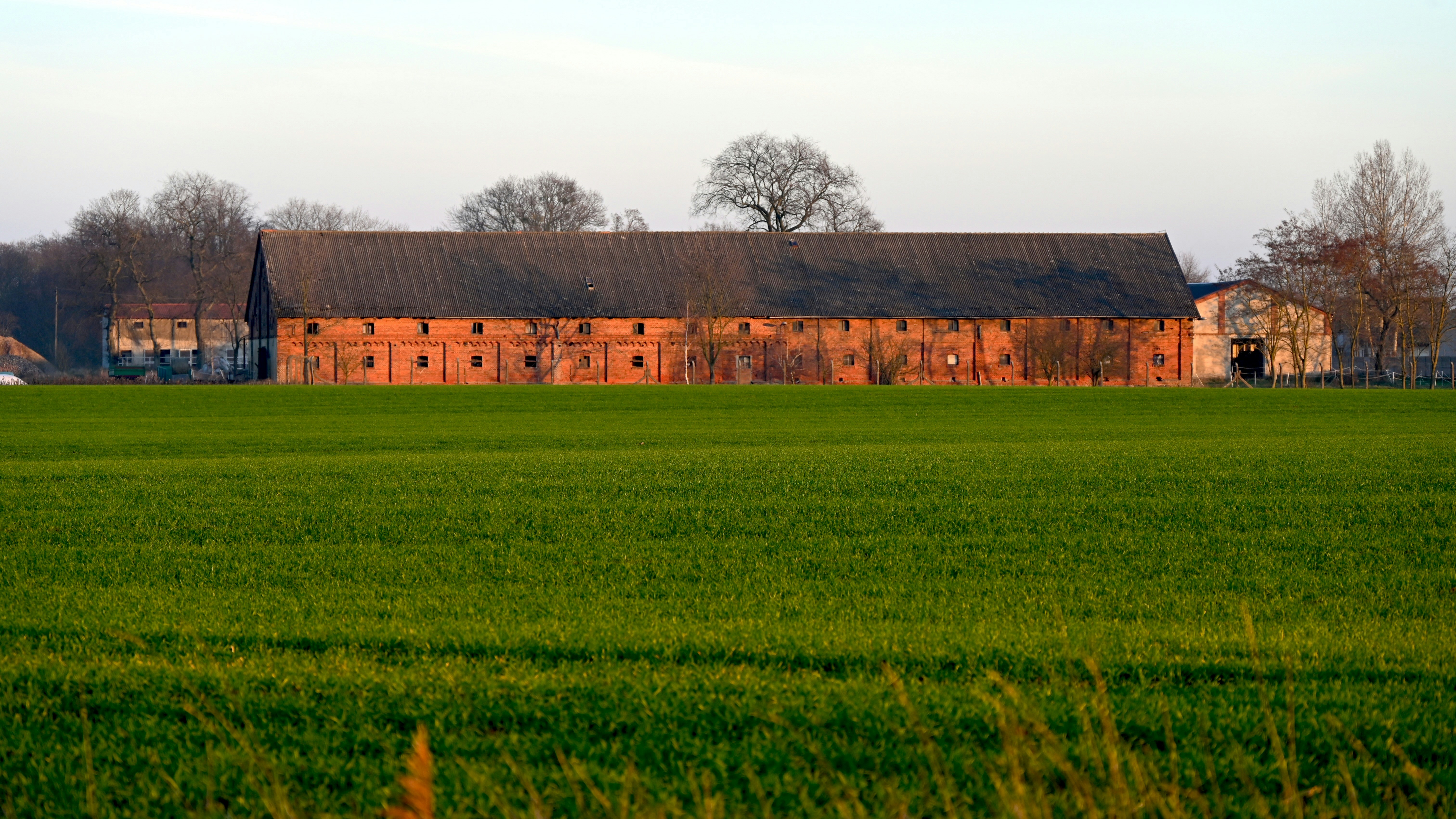 Long brick barn with houses and trees behind