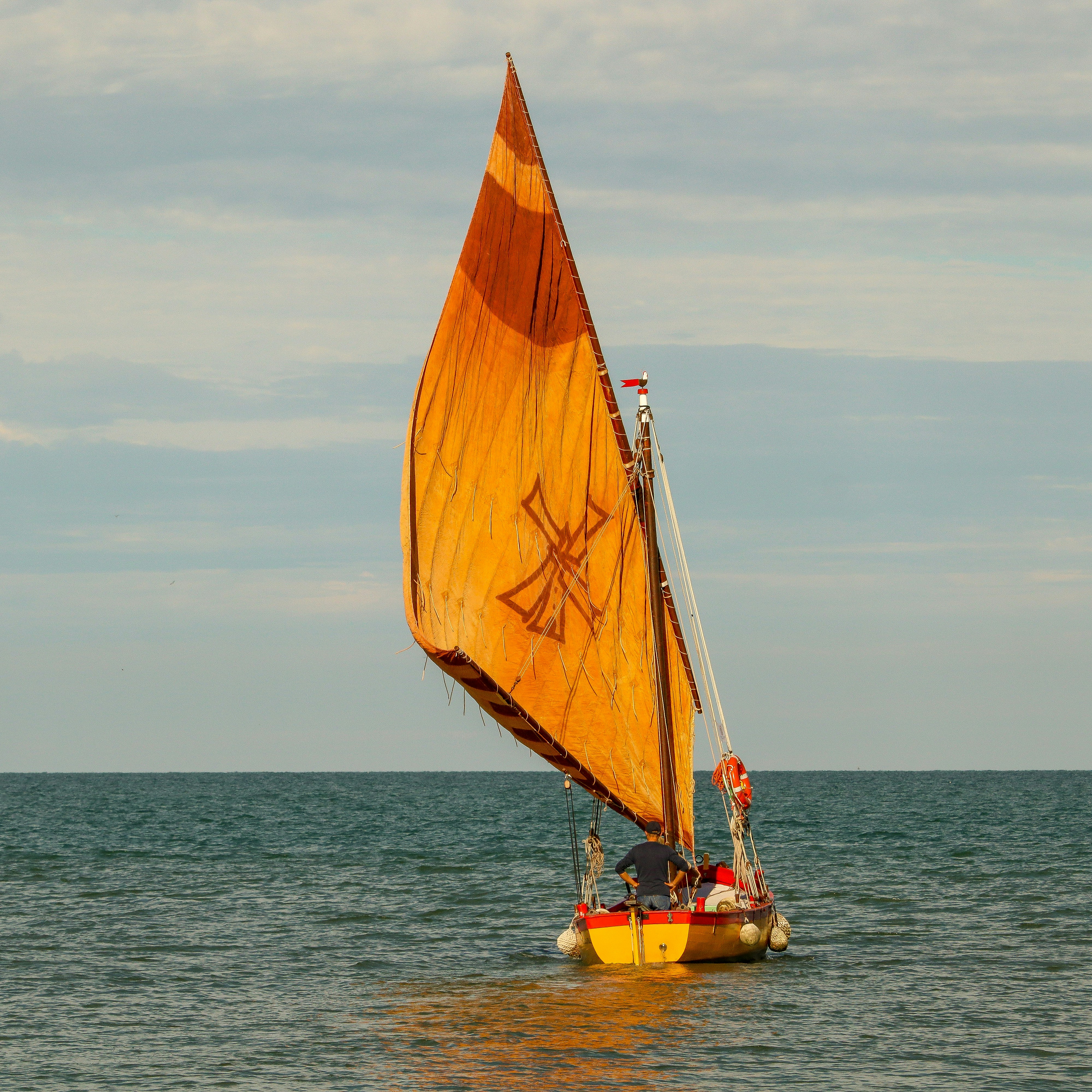 A yellow sailboat with an orange sail on the sea