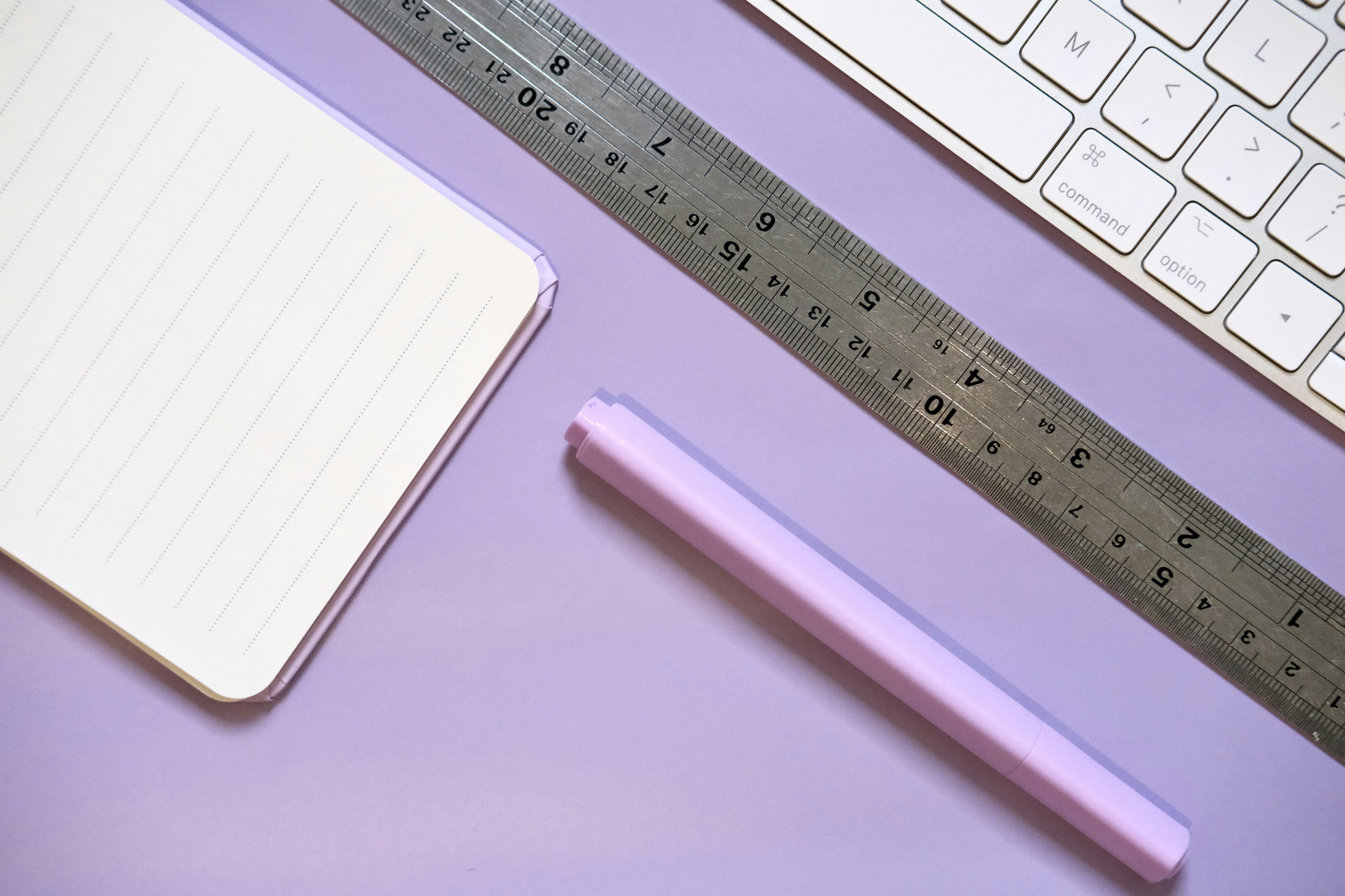 Notebook, ruler, pen, and keyboard on purple surface