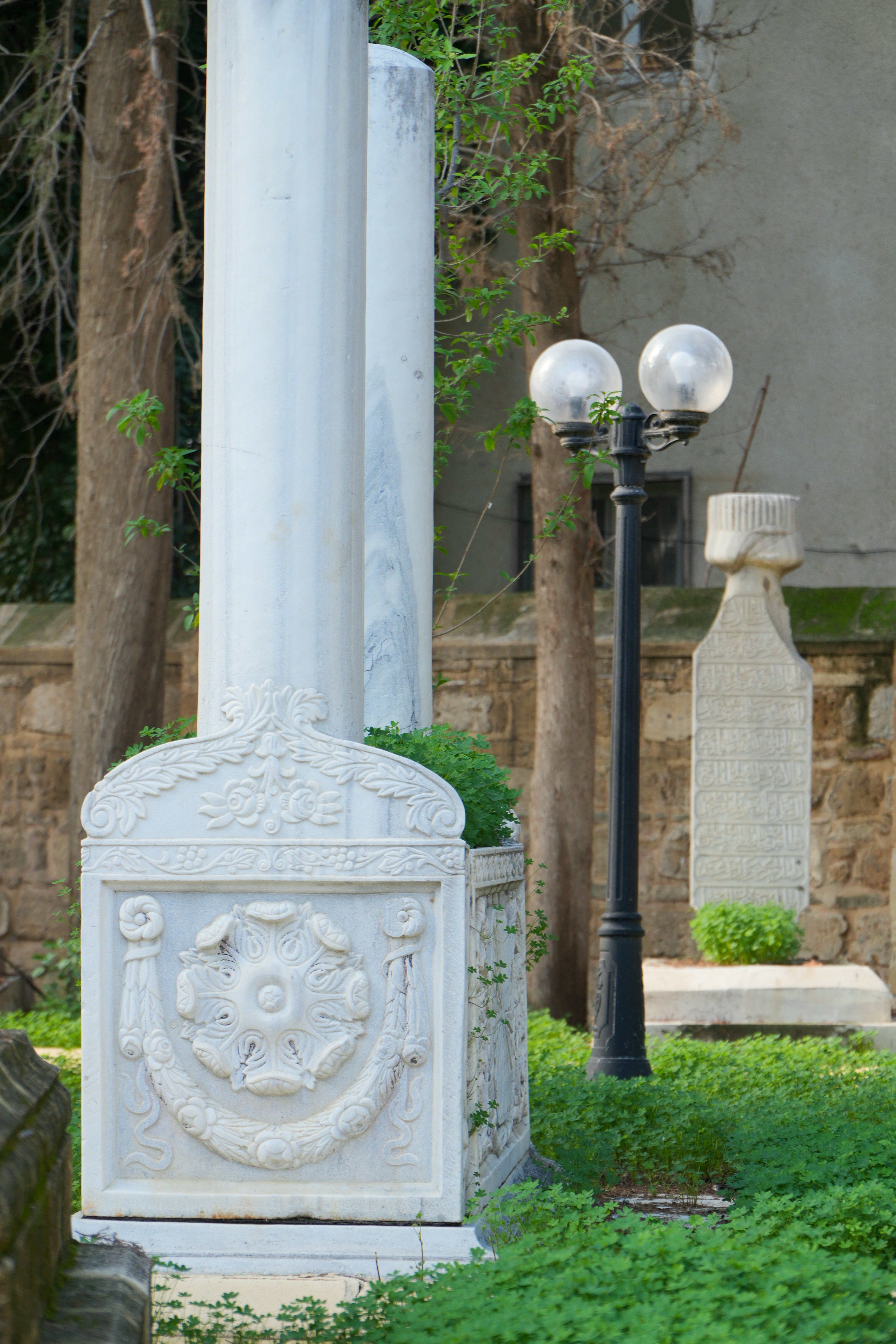 Ornate marble tombstone with lamppost and trees.