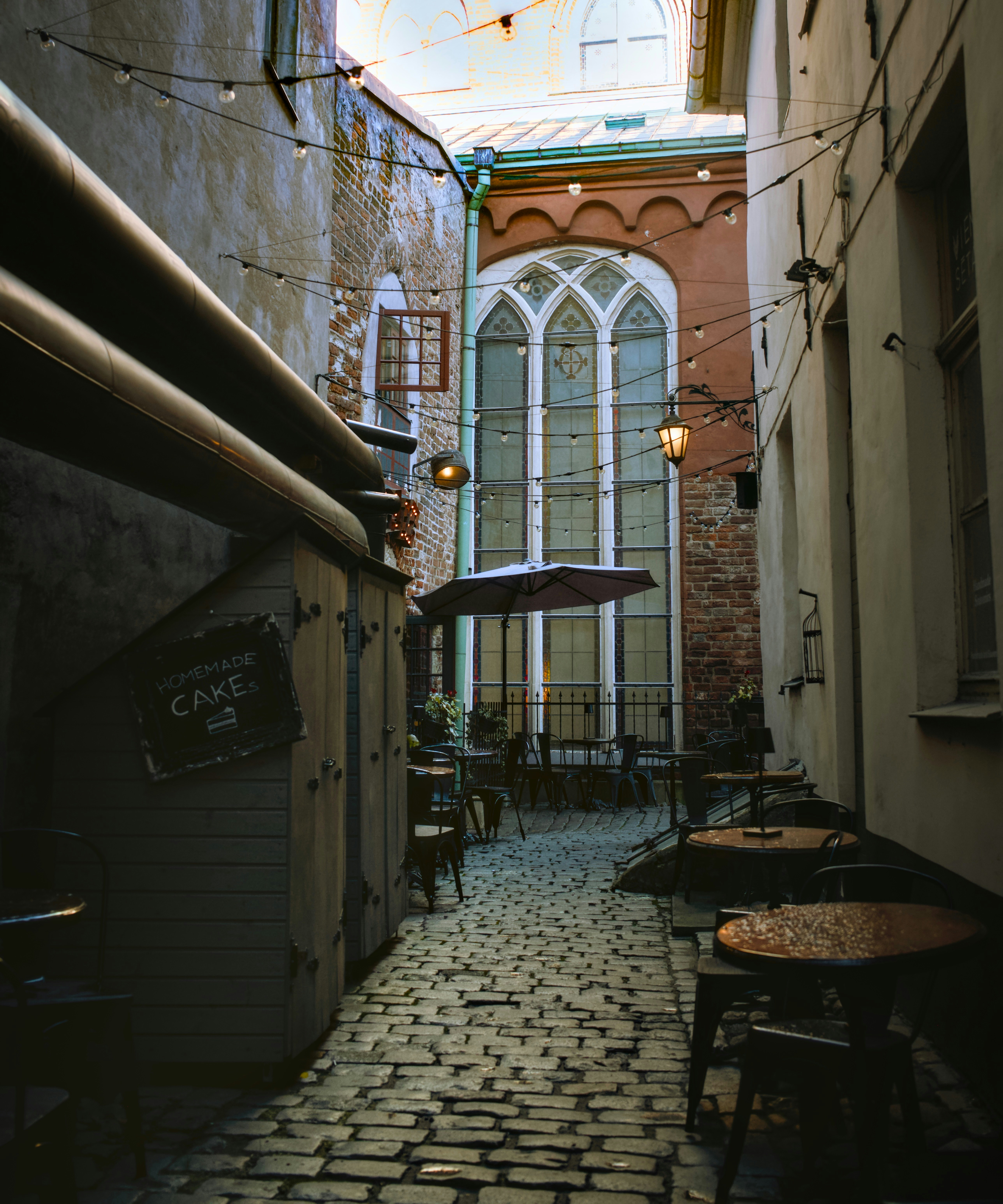 Cobblestone alley with outdoor cafe seating and arched window.