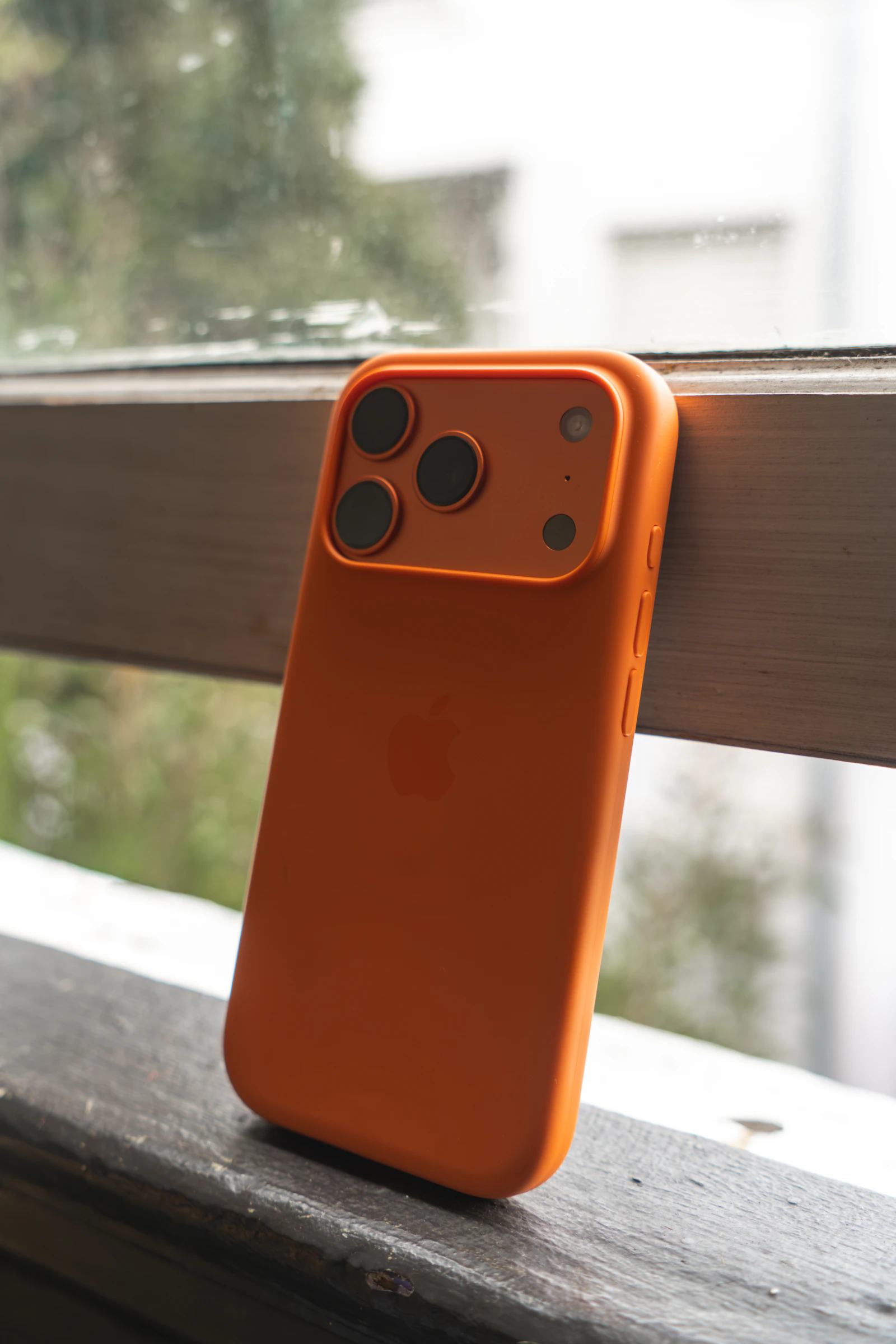 Orange protective smartphone case positioned beside a window
