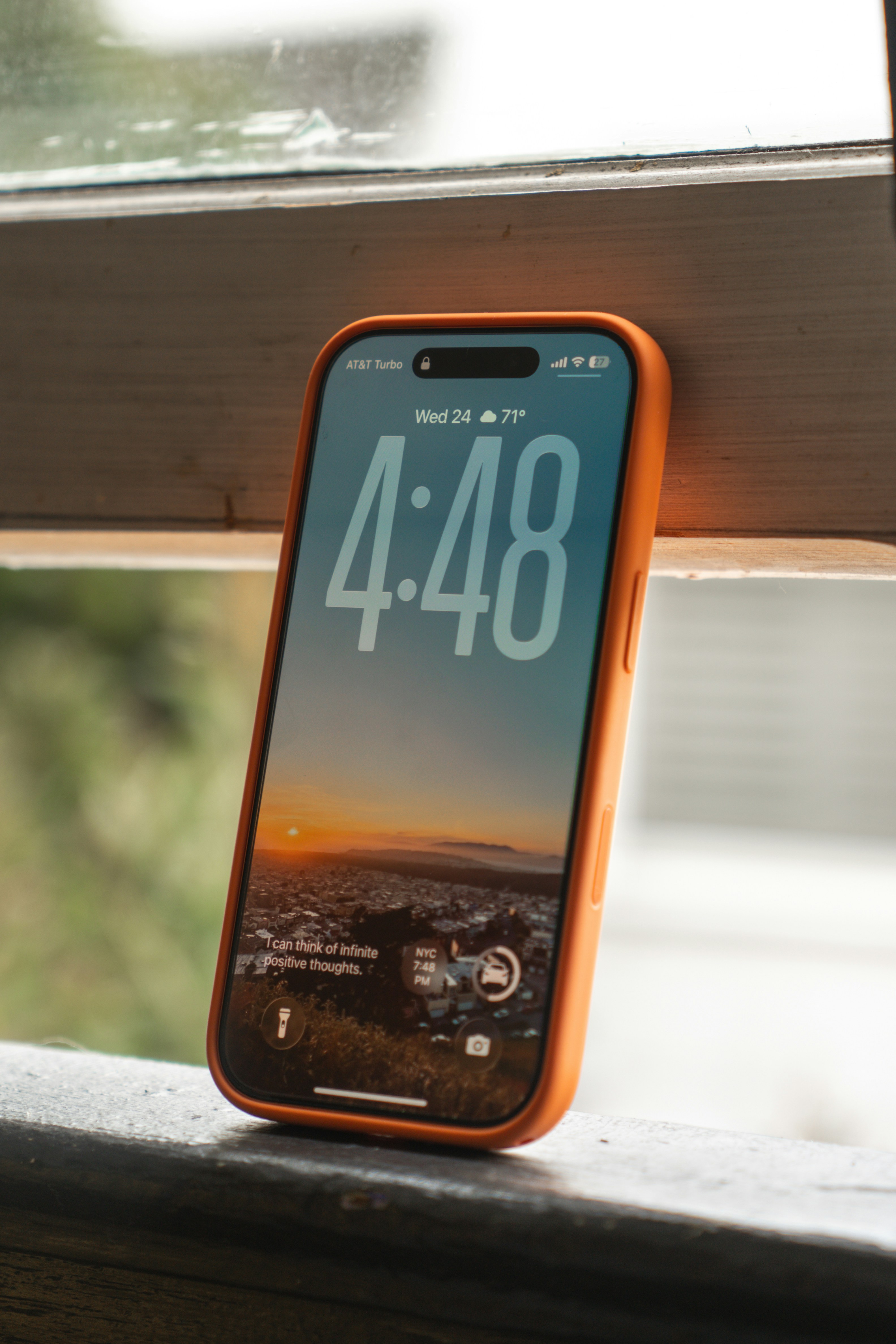 Smartphone con funda naranja que muestra fondo de pantalla al atardecer.