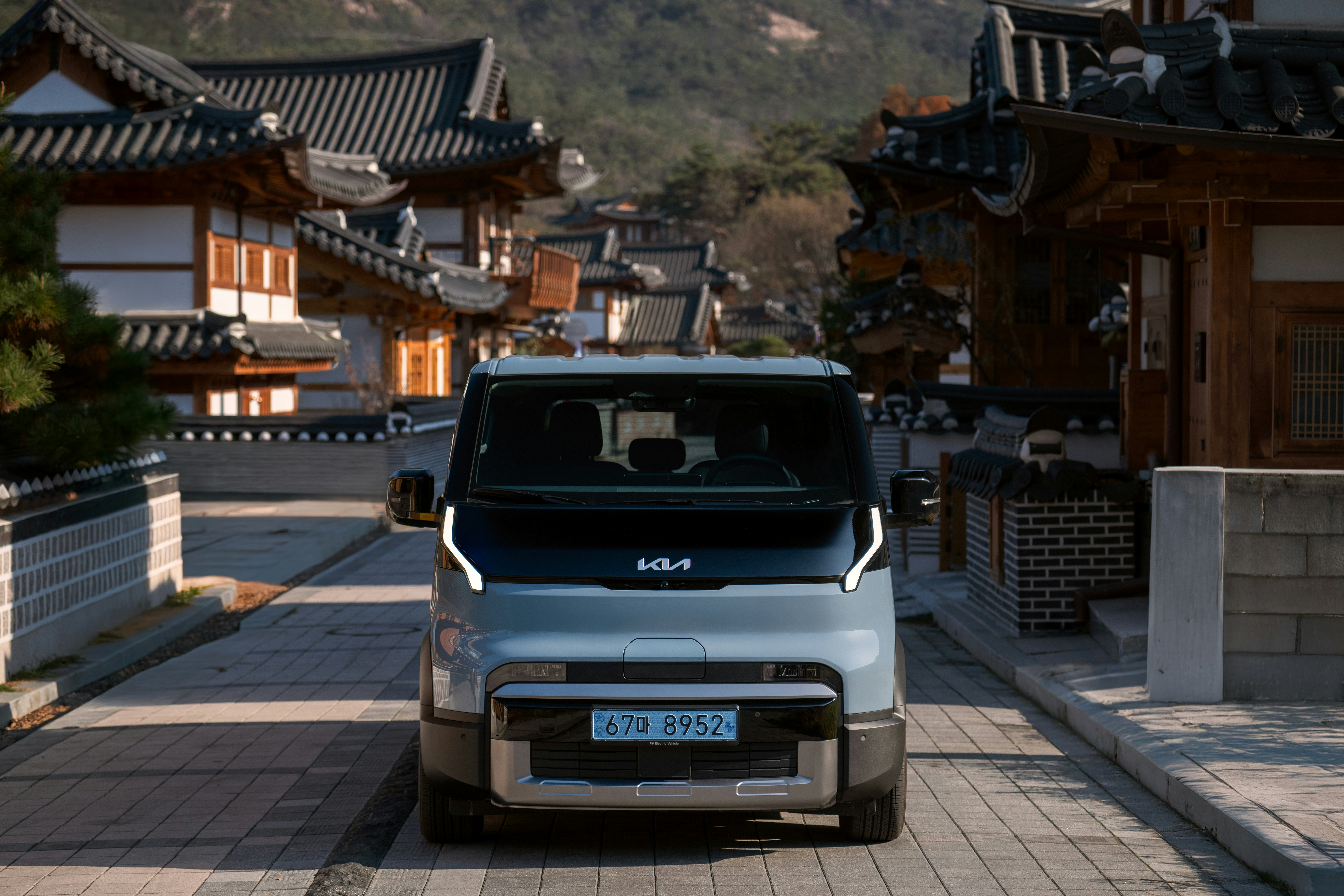 A modern kia van drives through a traditional korean village.