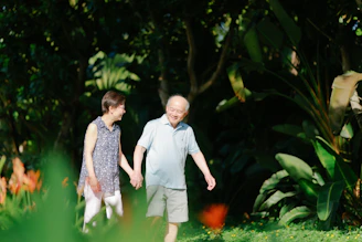 Elderly couple walking hand-in-hand in a lush garden.