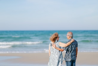 Elderly couple embracing on a sandy beach.