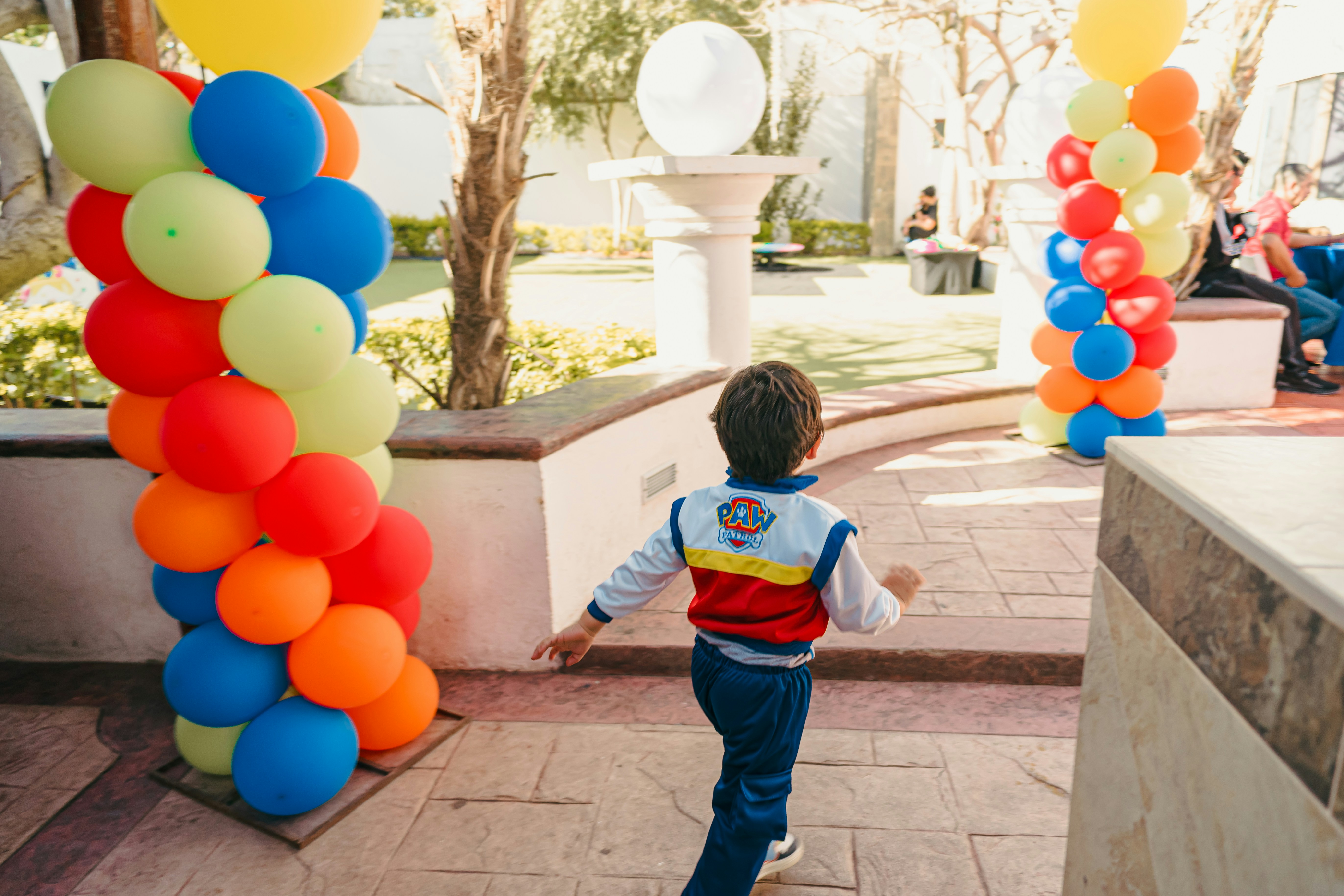 Boy in paw patrol jacket runs past colorful balloons