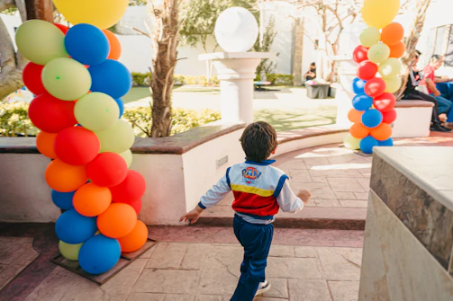 Boy in paw patrol jacket runs past colorful balloons