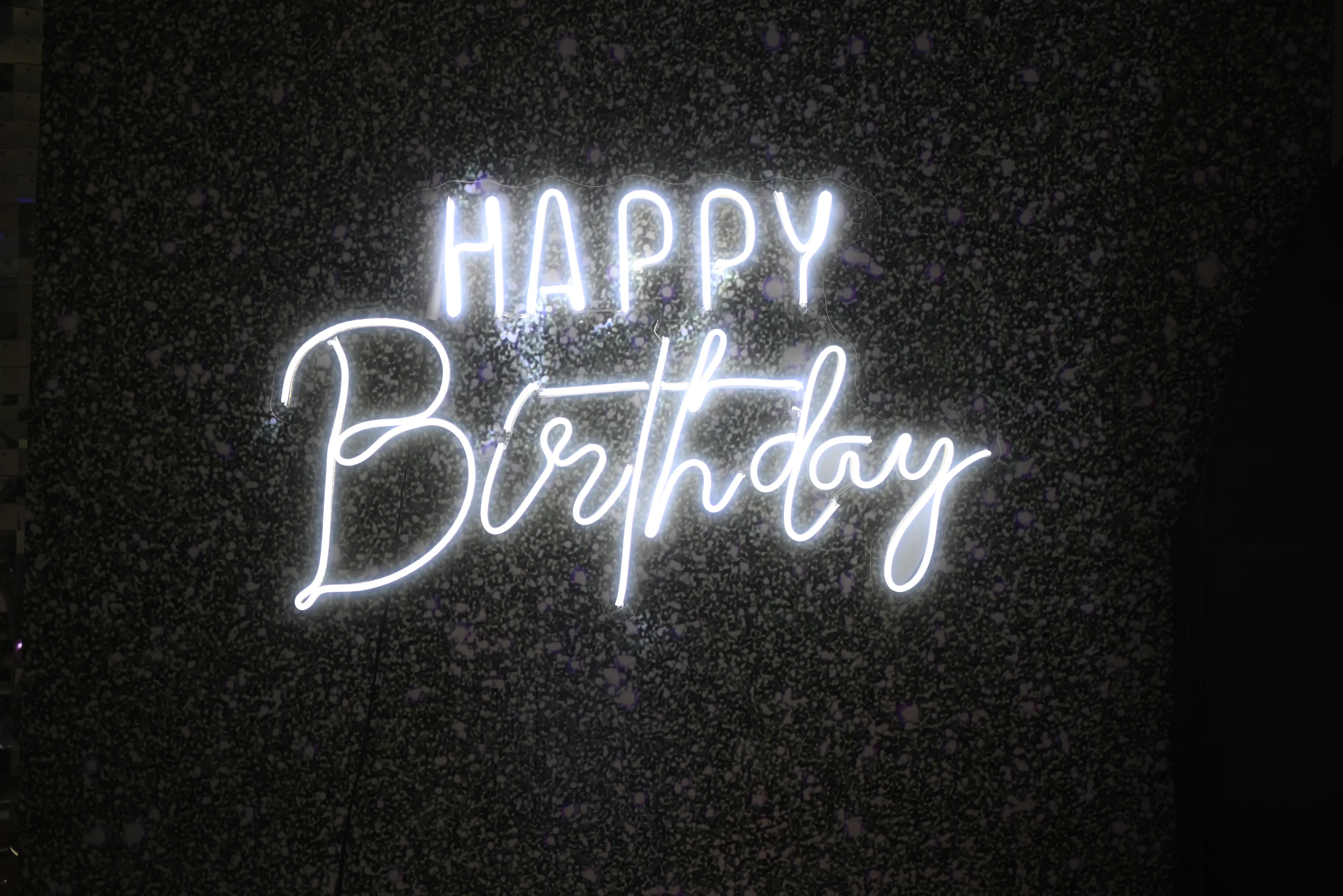 White neon Happy Birthday sign on a dark wall