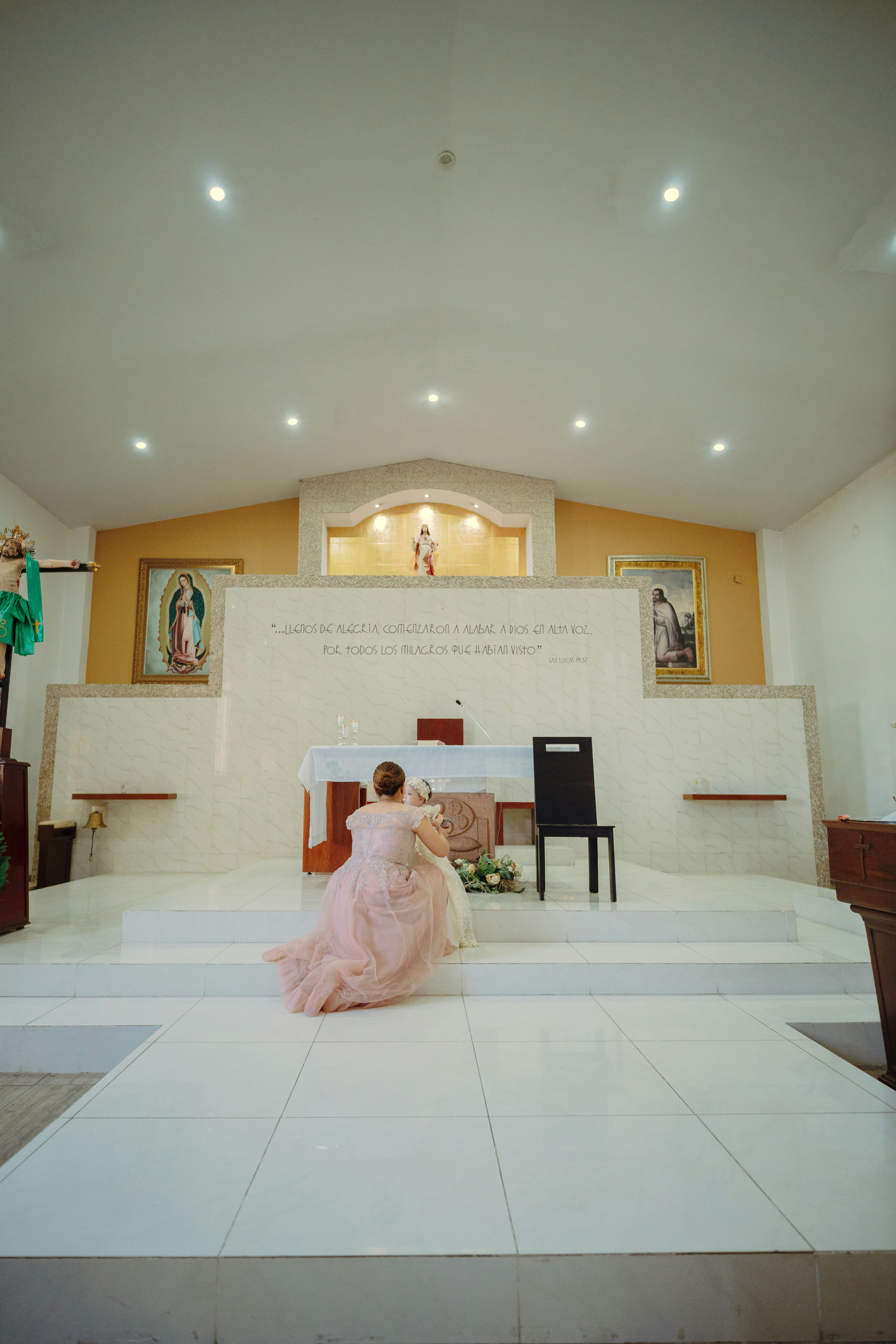 Mujer con vestido rosa arrodillada en el altar de la iglesia.