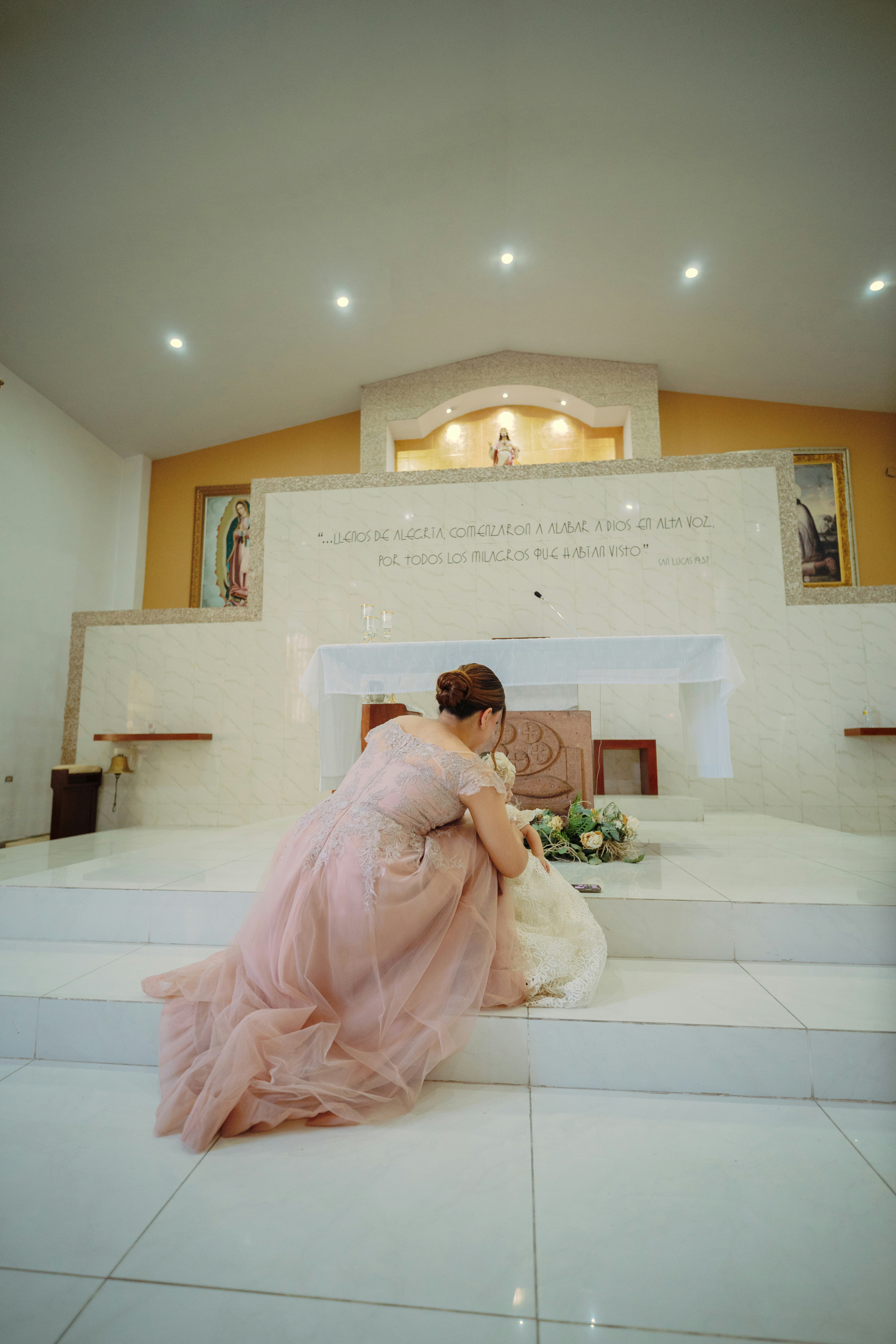 Mujer con vestido rosa arrodillada ante el altar con flores