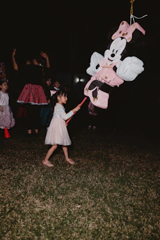 Young girl hitting a minnie mouse piñata at night.