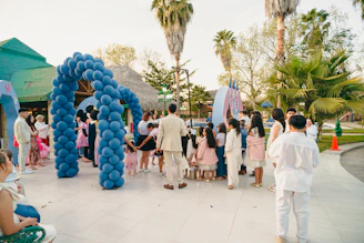People gather under a blue balloon archway outdoors