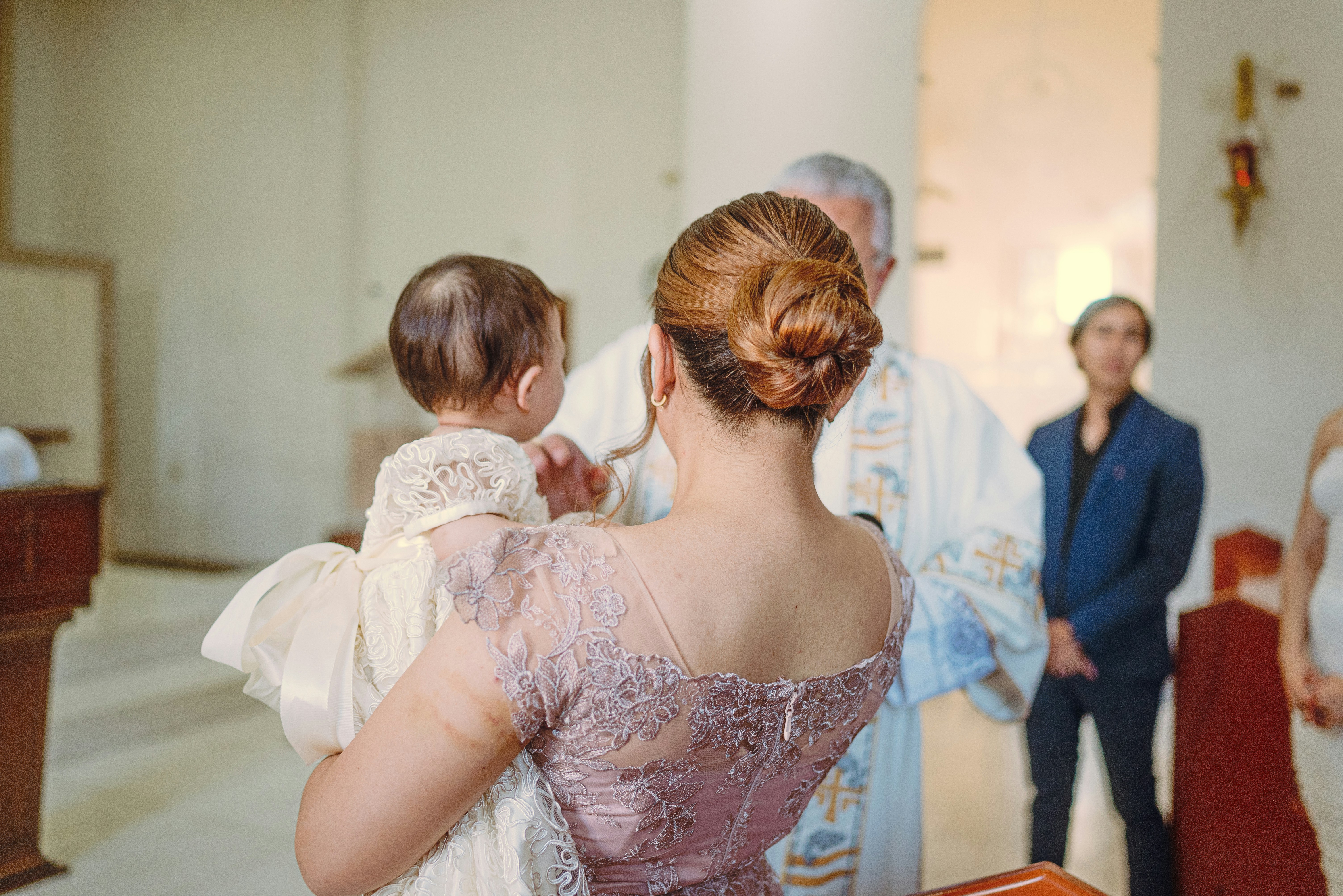 Mother holds baby during baptism ceremony with priest.