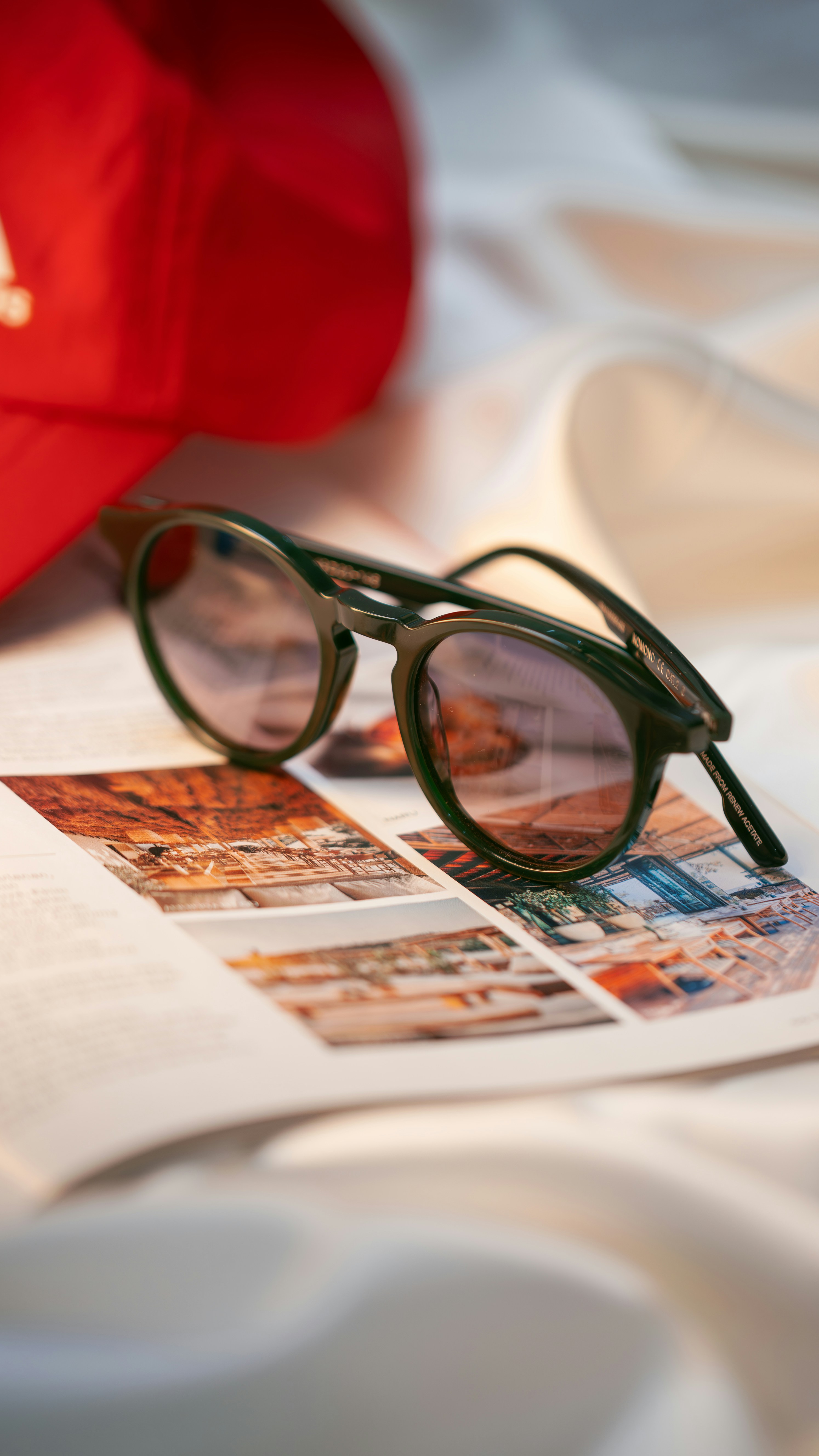 Óculos escuros verdes repousam sobre uma revista ao lado da tampa vermelha.