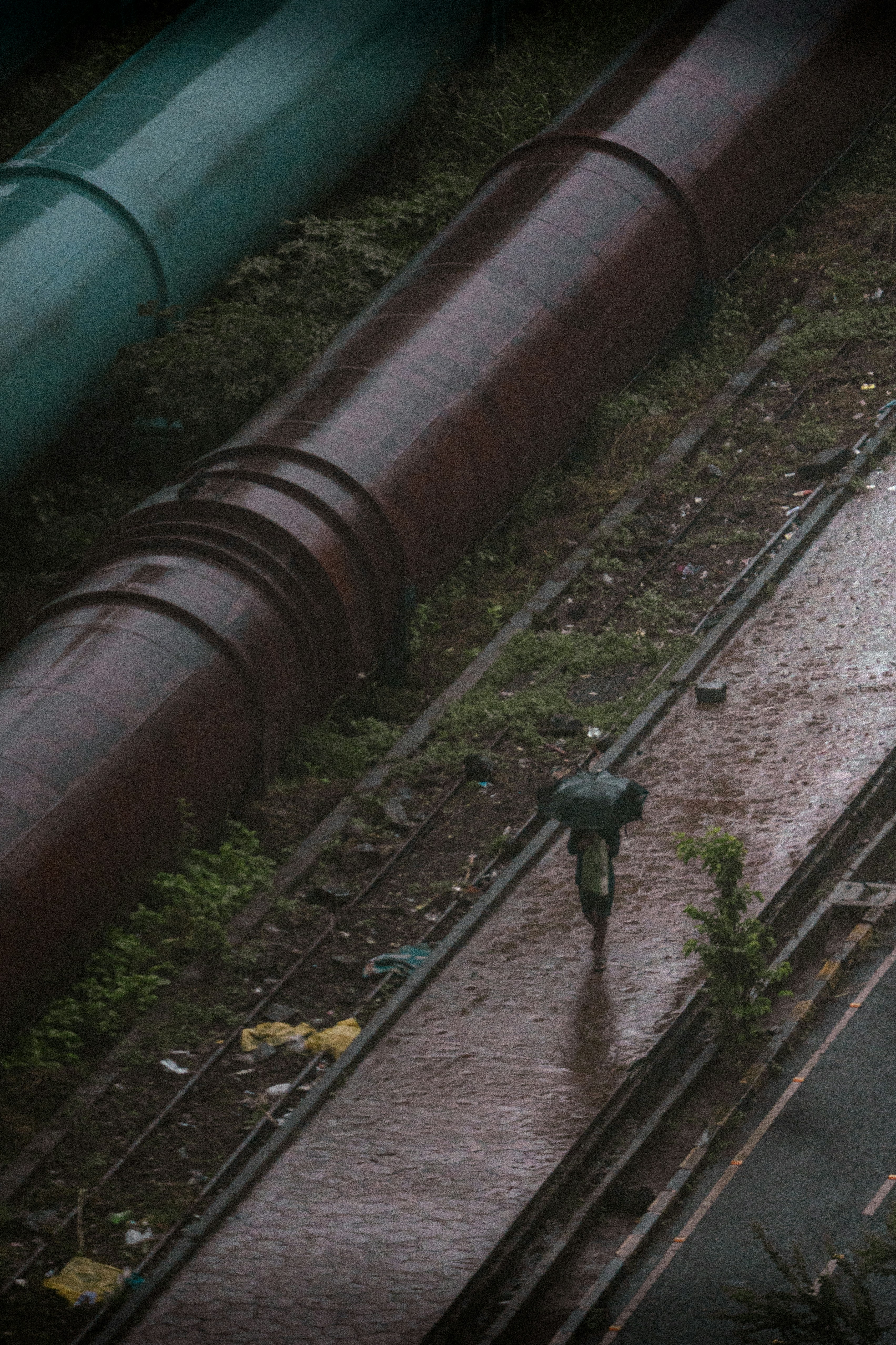 Person with umbrella walks past large pipes in rain