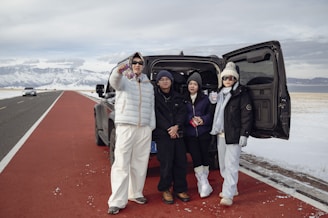 Four people standing by a car in a snowy landscape.