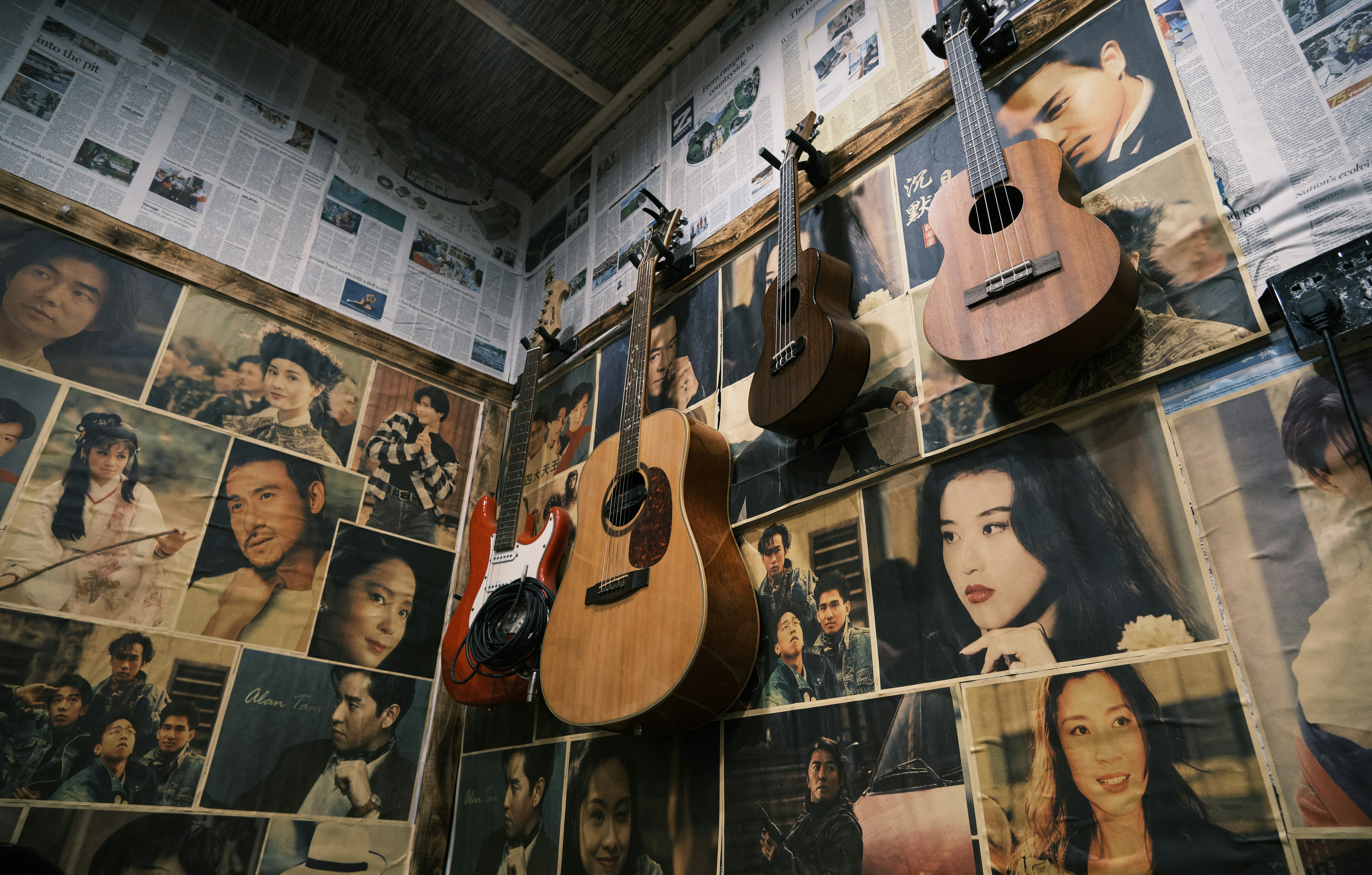 Guitars and ukuleles hang on a wall covered in photos.