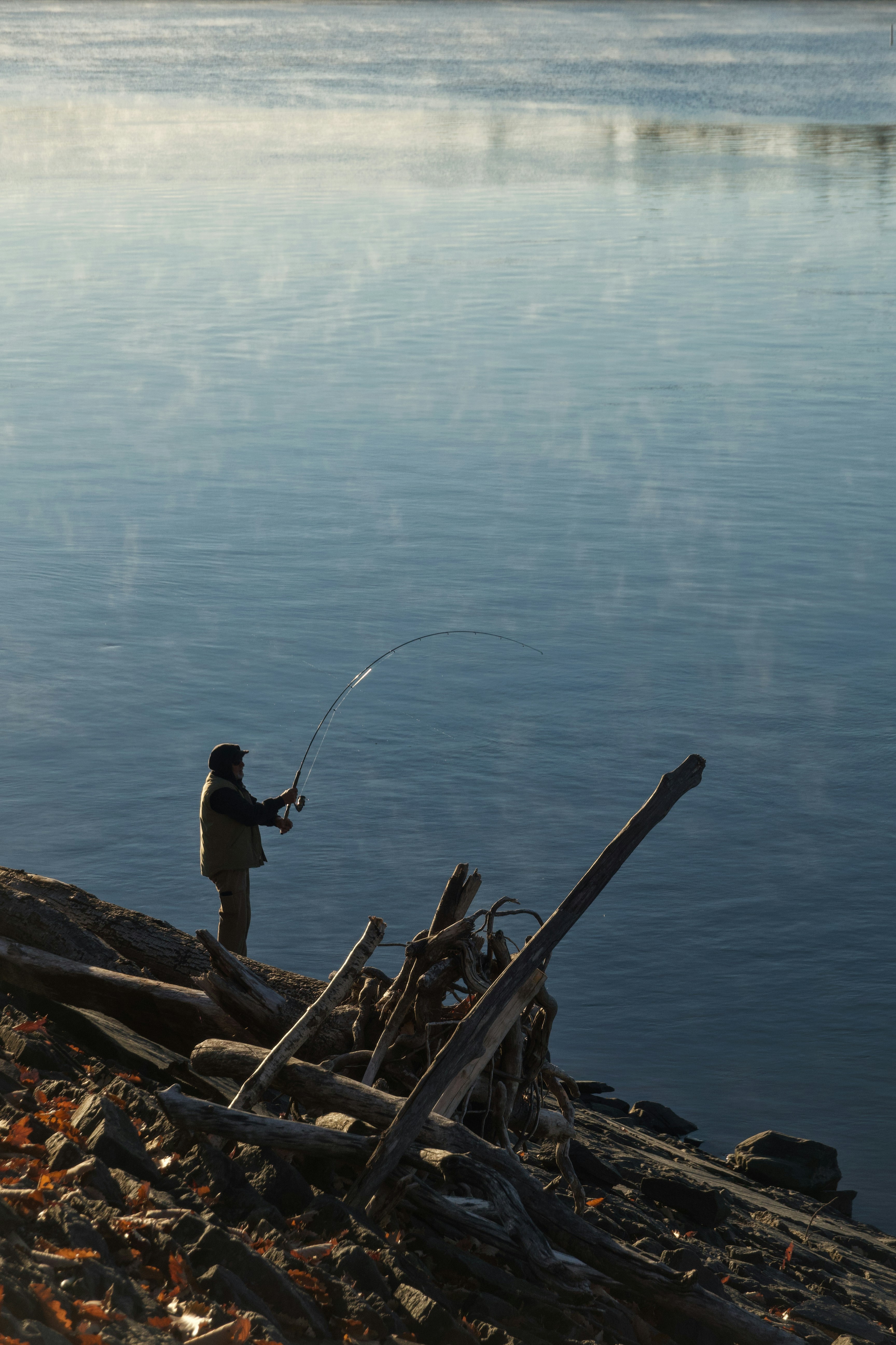 Man fishing from a rocky shore with driftwood