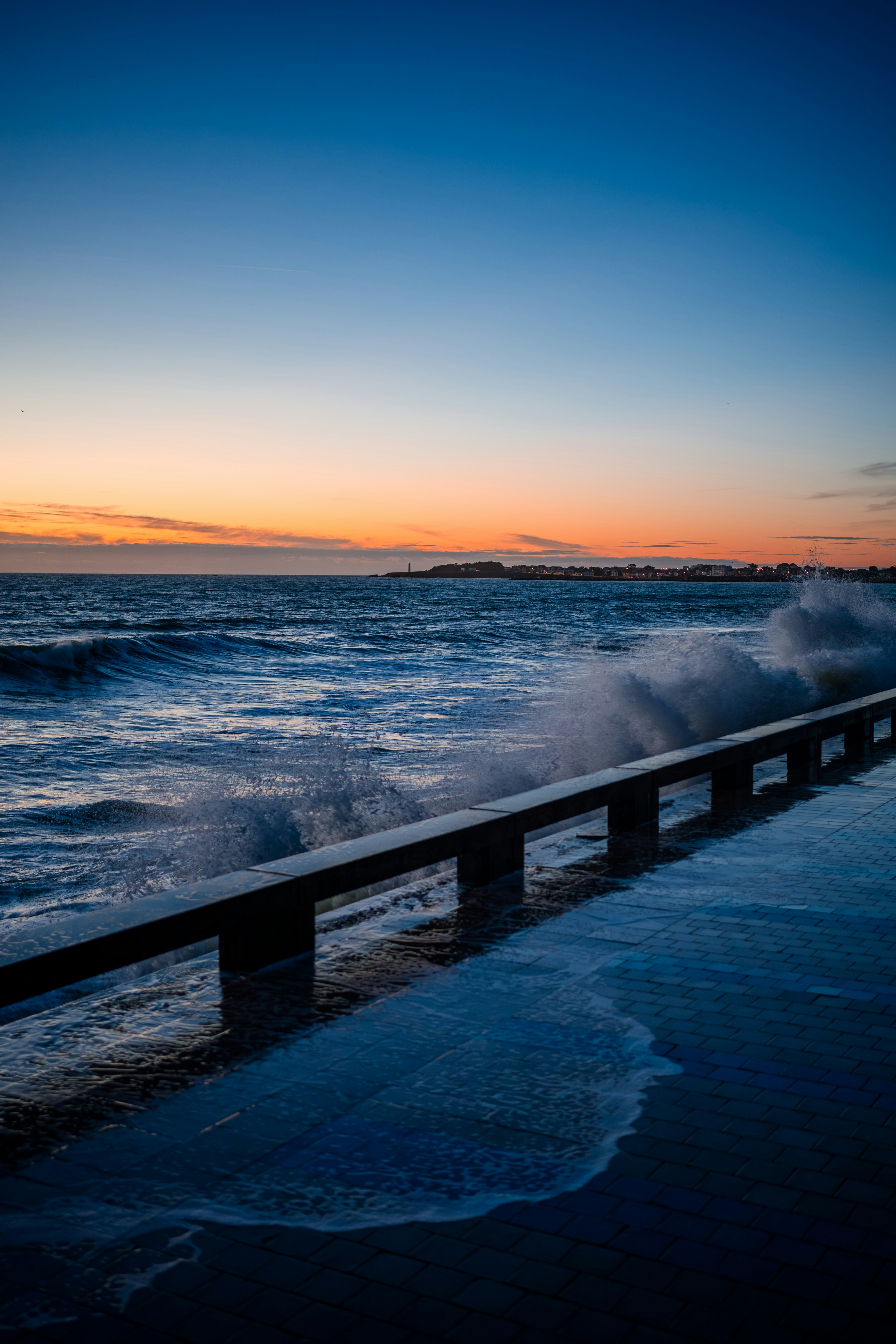 Waves crash against a pier at sunset.