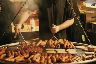 Man grilling many sausages and burgers on a large grill.