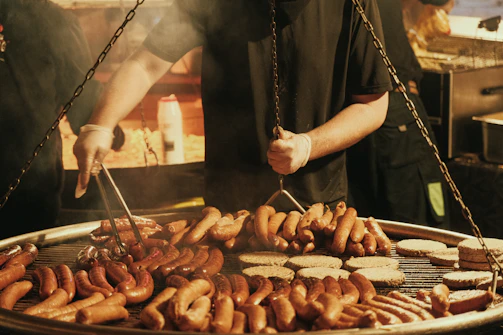 Man grilling many sausages and burgers on a large grill.