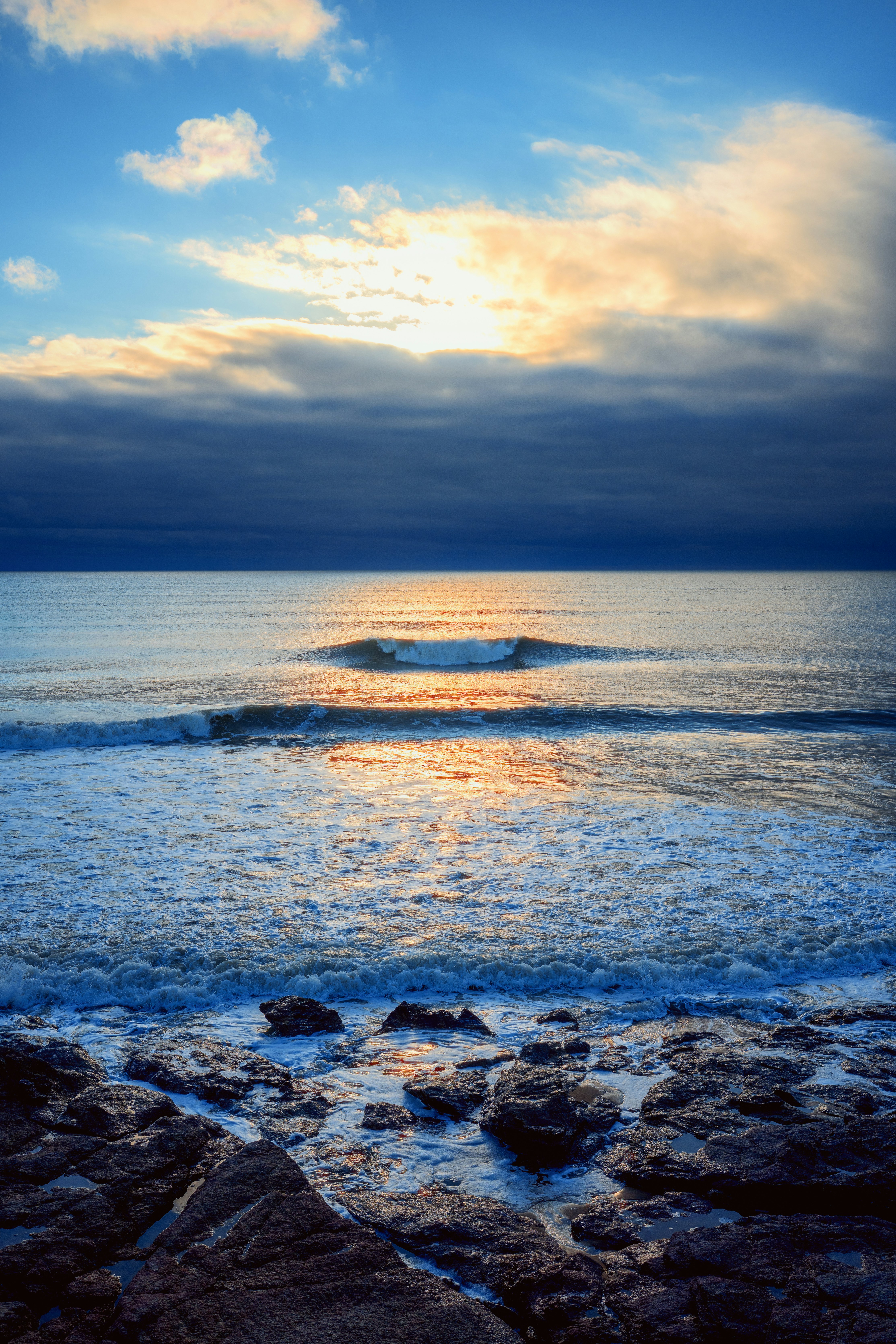 Ocean waves crash on rocky shore at sunset.