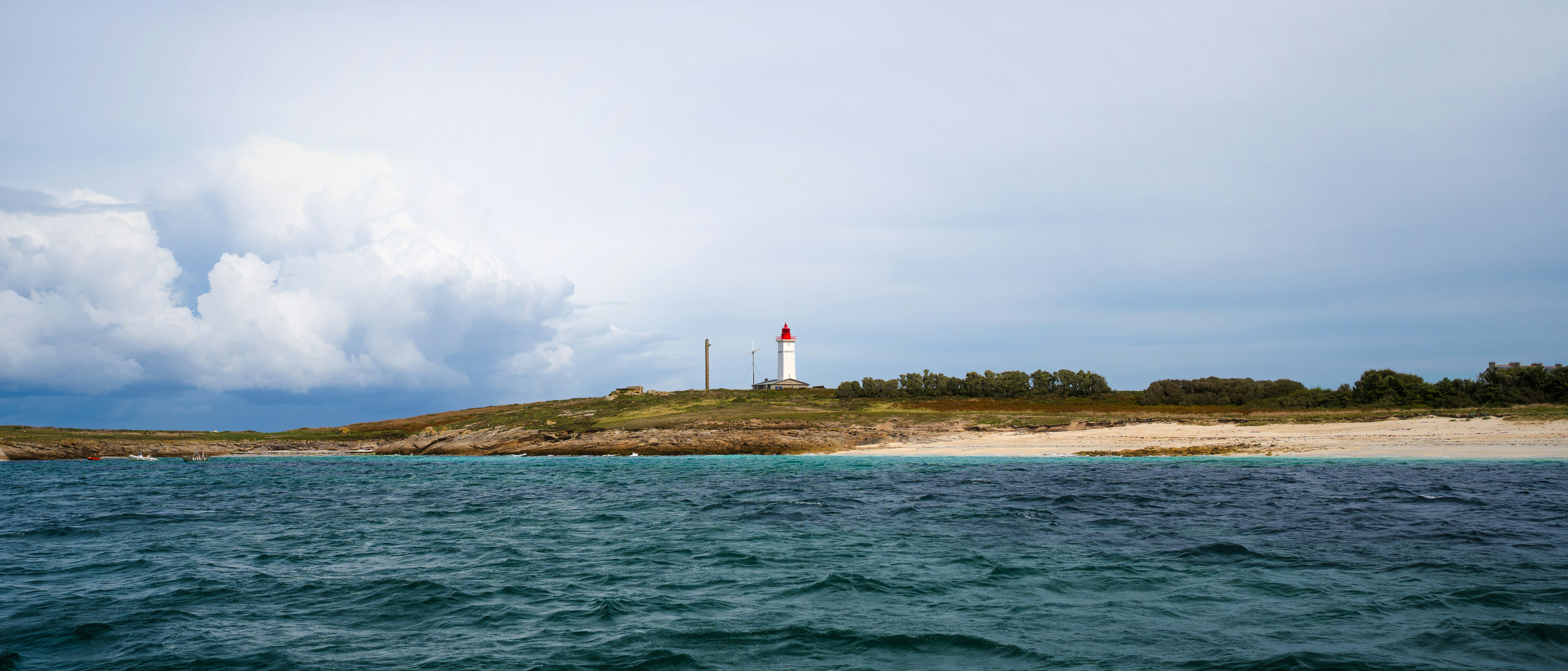 Lighthouse on a sandy shore with choppy blue water.