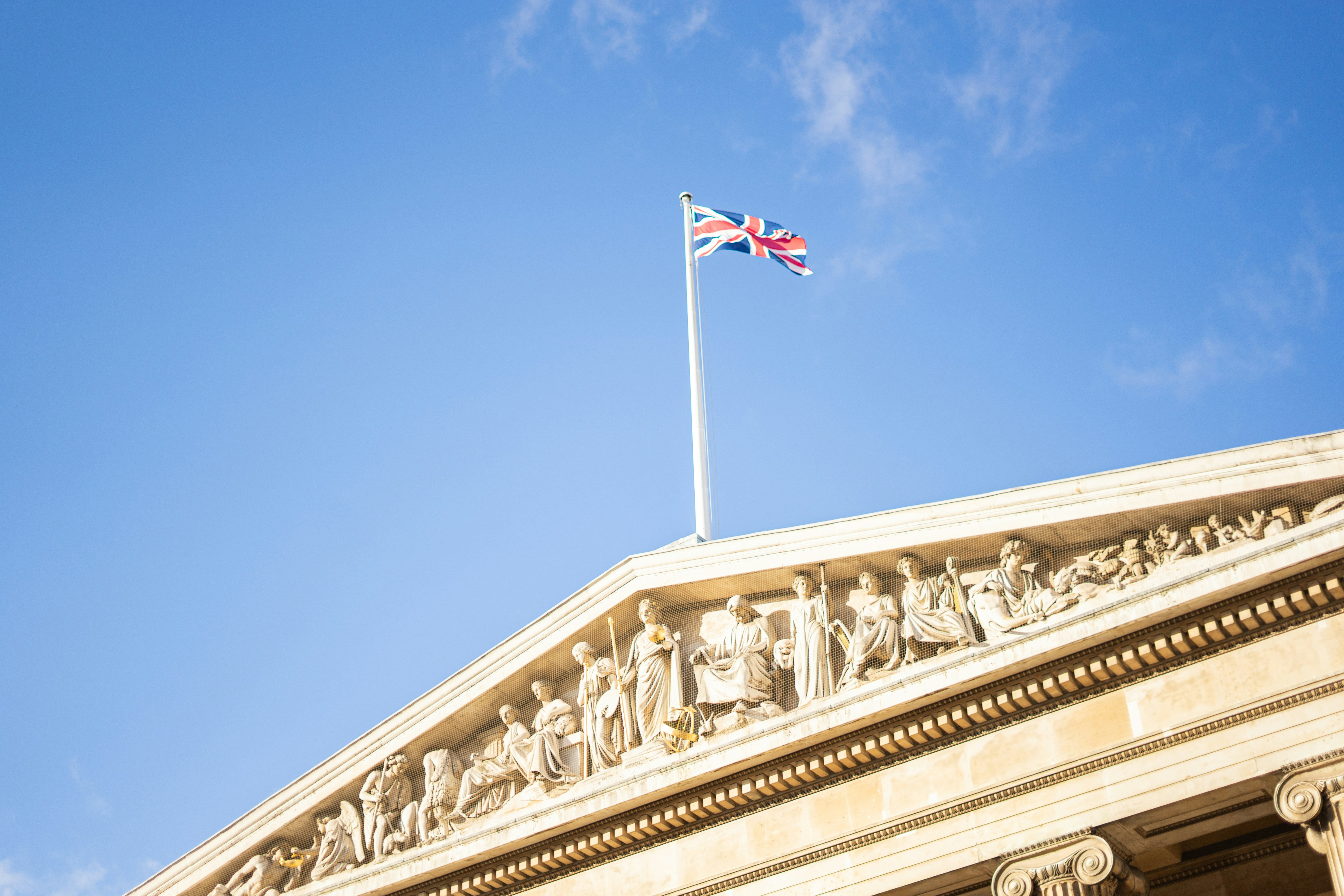 Union jack flag flying above a classical building facade.