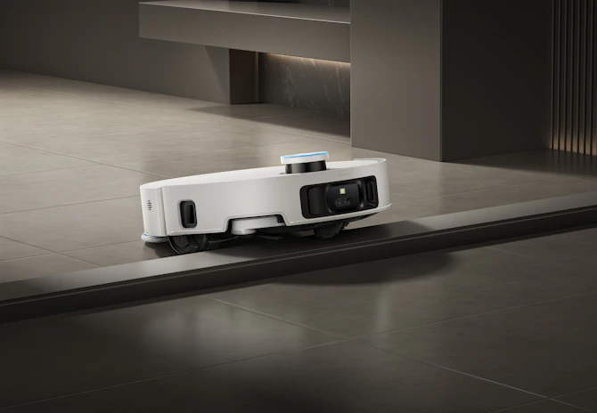 A white robot vacuum cleaner navigates a floor transition.